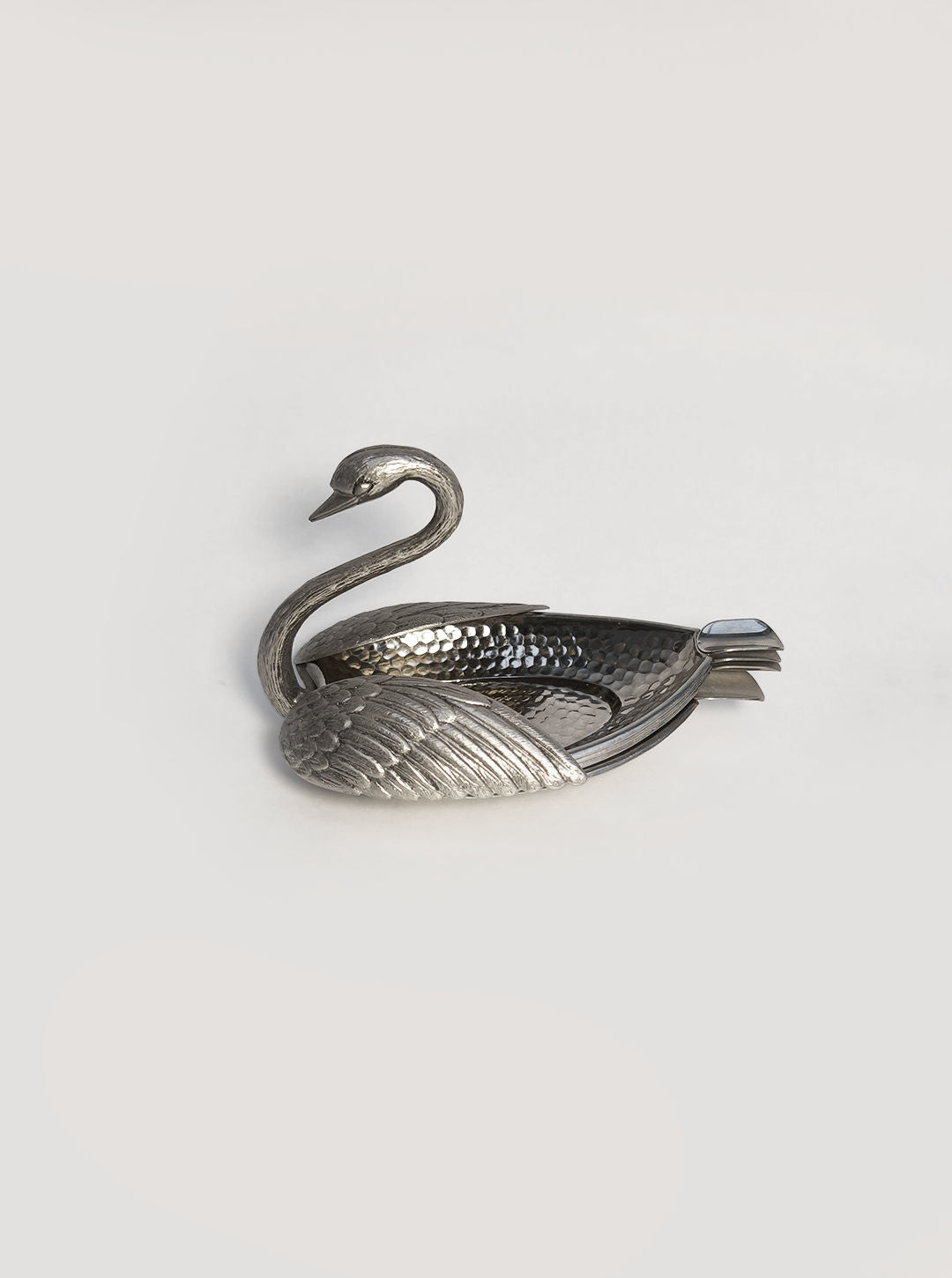 A Swan Ashtray by Les Objoies, featuring a metallic swan shape with a textured surface, sits on a light gray background. Its long neck curves elegantly upwards, and detailed feather patterns adorn the body, making it an ideal sophisticated metallic centerpiece for any kitchen or dining area.