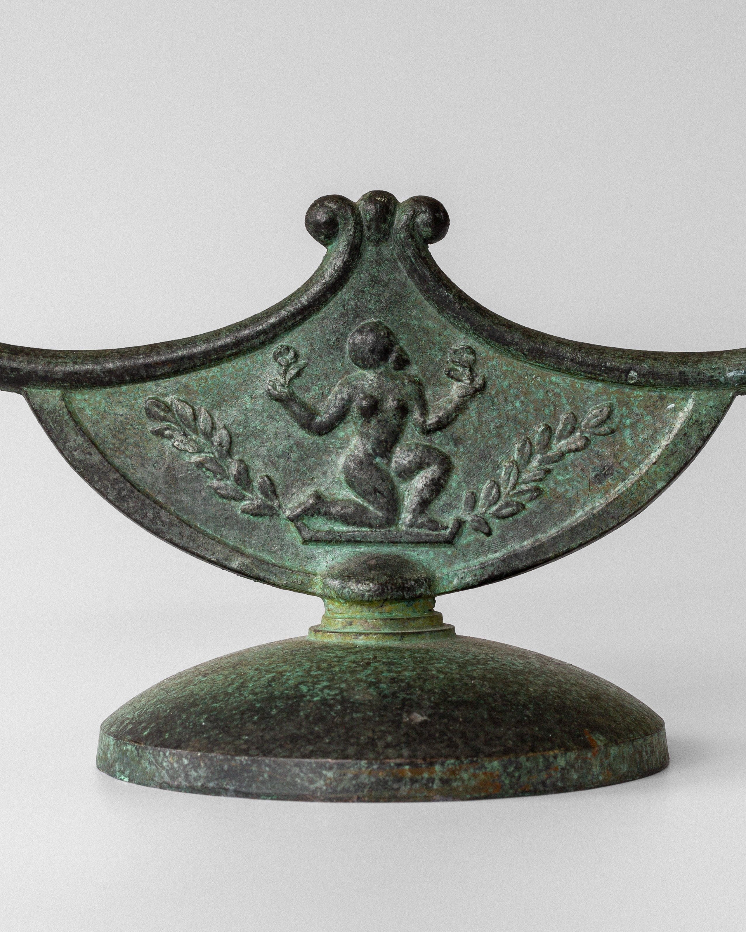 A close-up of a decorative Art Deco green metal object by Spigel, featuring an intricate relief with a figure and leaf motif, finished in patinated bronze. Its wide, rounded base evokes classic Swedish metalwork.