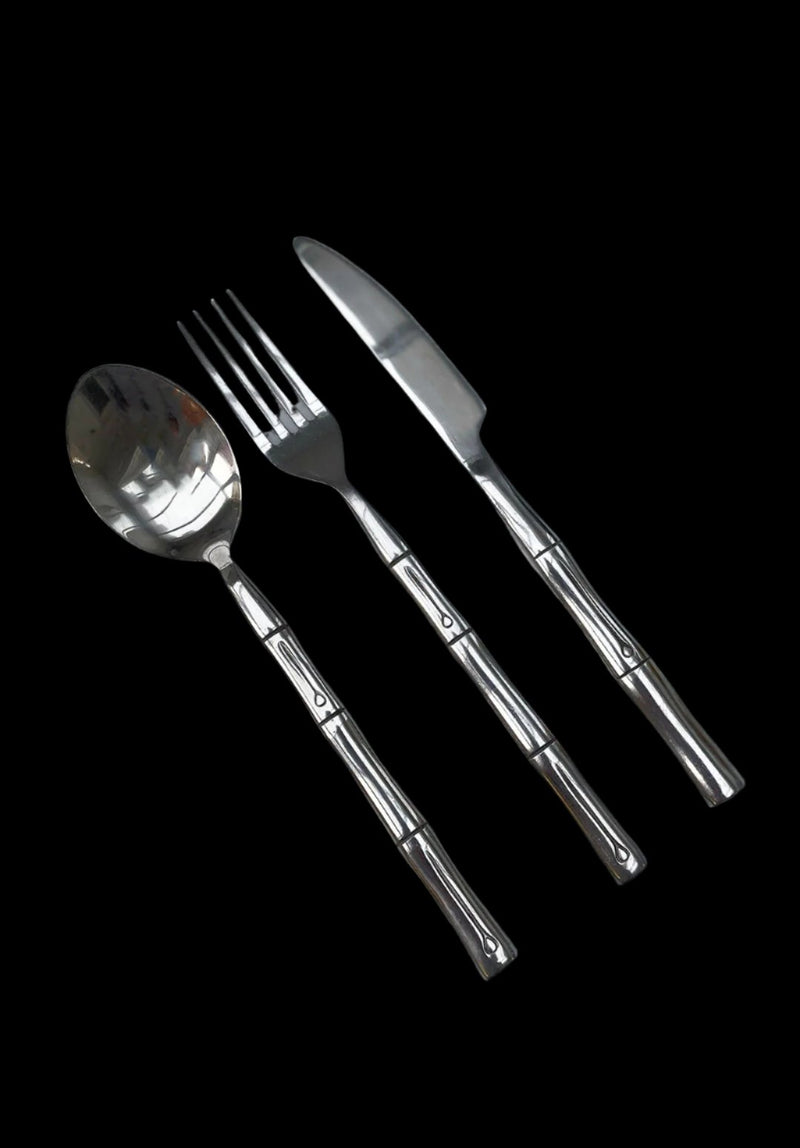 A set of bamboo cutlery from Les Objoies, consisting of a spoon, a fork, and a knife arranged side by side against a black background. The handles feature a distinctive linear design with small decorative elements, perfect for exotic table settings.