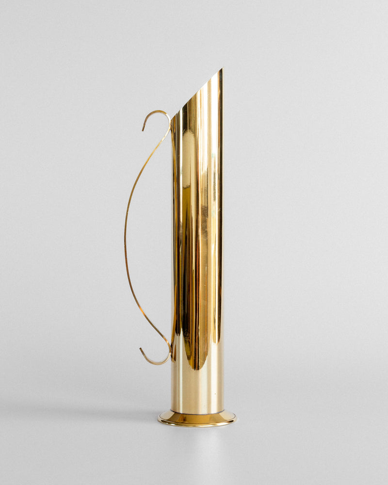 The Spigel Large Mid-Century Brass Vase, tall and cylindrical with a narrow spout and curved handle, stands on a flat surface against a plain light gray background, evoking Scandinavian modernist elegance.