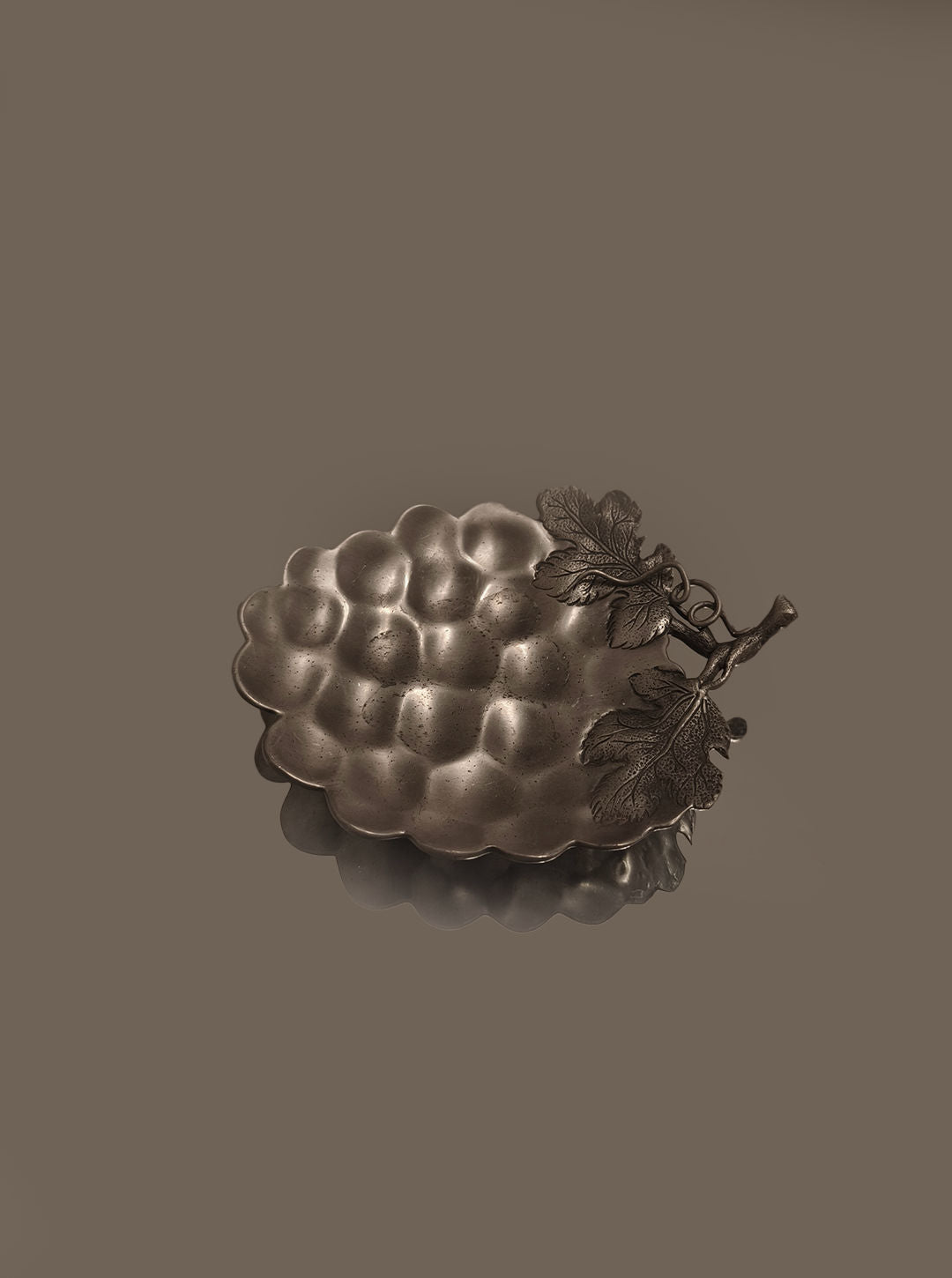 Introducing the Grape Vide Poches by Les Objoies, a bronze-colored ornamental dish featuring an intricate grapevine motif with detailed leaves and stem set against a plain background. This decorative piece exudes elegance and charm, making it perfect for enhancing any space.