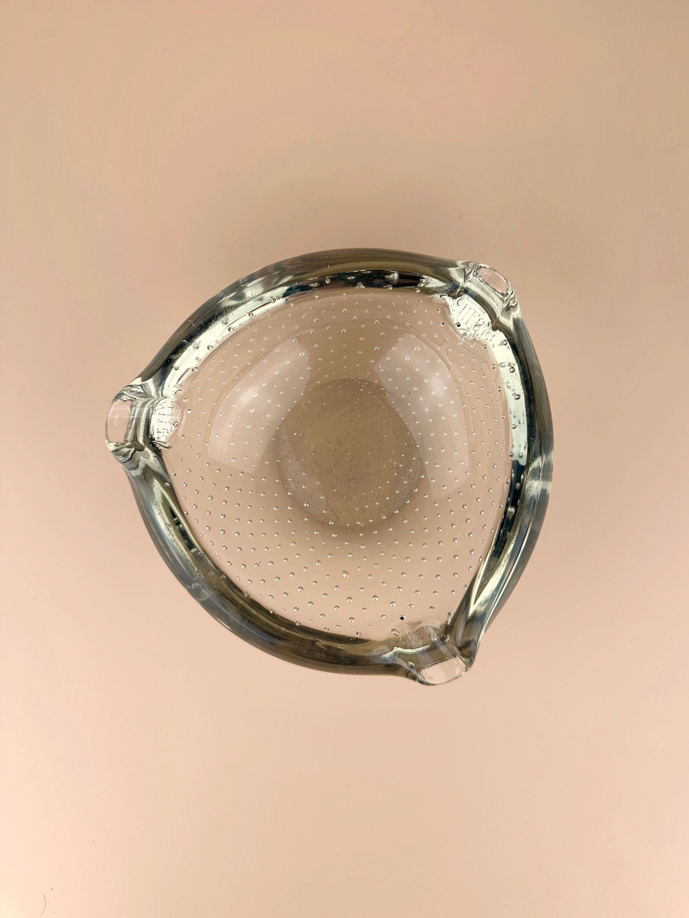 A transparent citrine glass 1950s yellow Murano Bullicante ashtray by Dodo Vintage with small raised bumps and three spouts, set against a plain, light pink background. The ashtray's simple and sleek design is reminiscent of a 1950s ashtray, clearly visible from a top-down perspective.