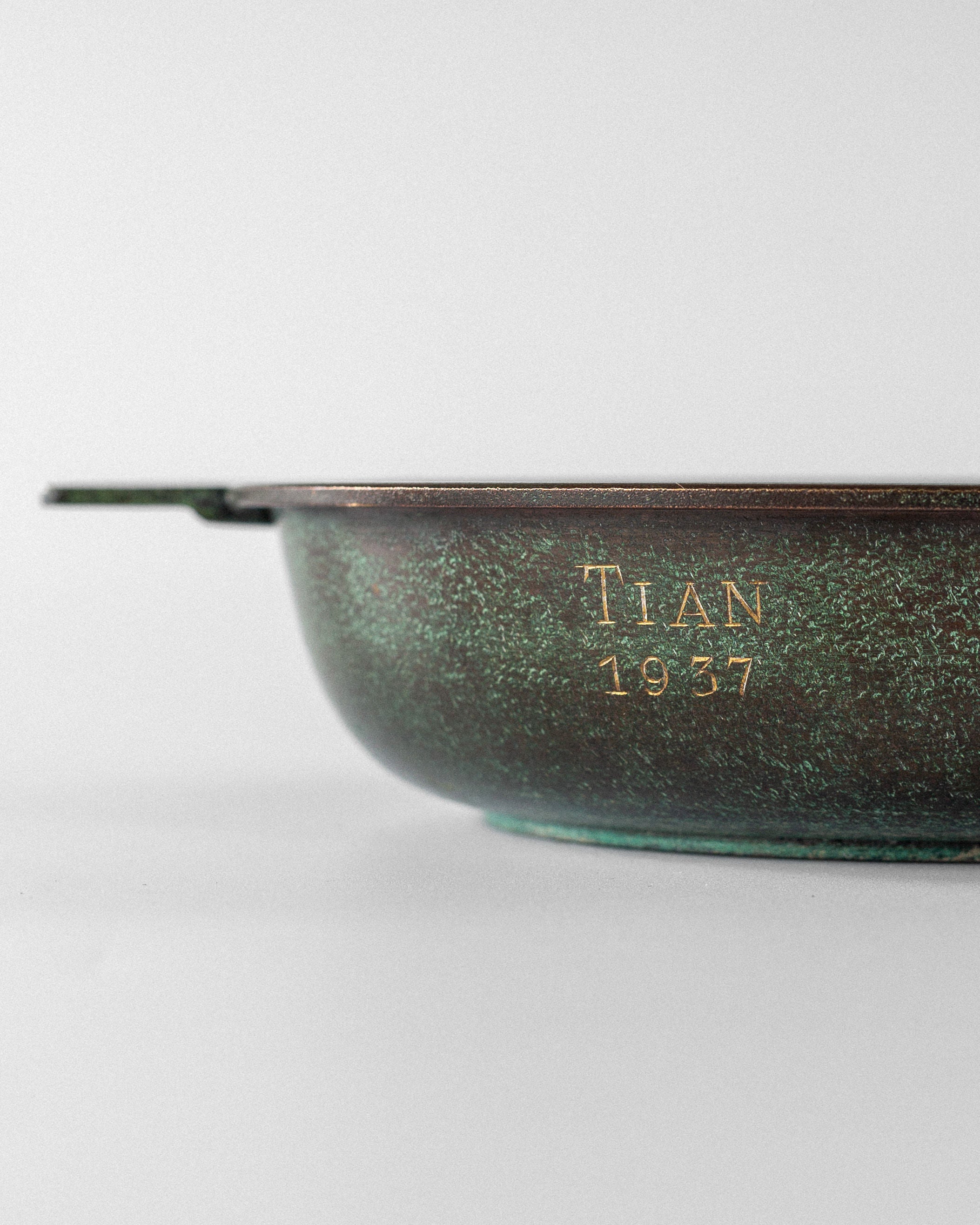 Close-up of a tarnished Art Deco bronze bowl by Spigel, Sweden 1930s, with "TIAN 1937" engraved on its side. It features Greek key handles and greenish patina, set against a plain, light background.