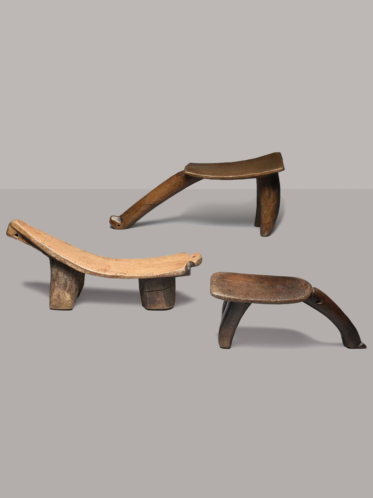 Three Lobi Tripod Stools from RELIC LONDON, each featuring distinct traditional wooden designs, are displayed against a plain, neutral background. Each stool showcases unique forms with curved and angled features that highlight the craftsmanship and cultural significance. These vintage pieces evoke the rich heritage of Burkina Faso.