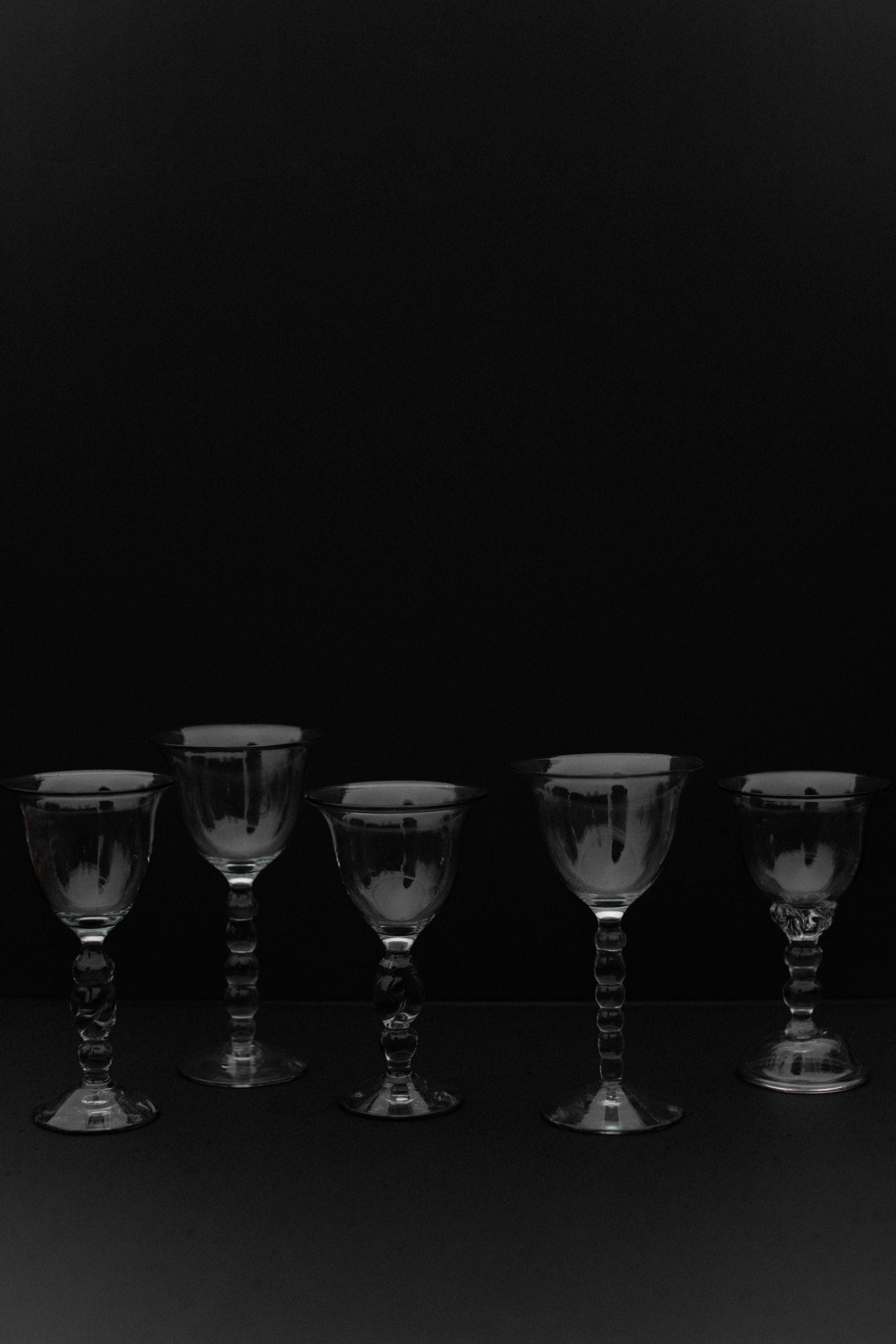 Five handmade art glasses from Out For Lunch are symmetrically arranged against a black background, casting subtle reflections. Their exquisite craftsmanship and varying shapes and sizes highlight their unique beauty as decorative accents.