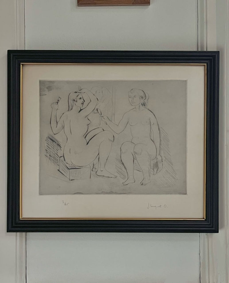 Framed artwork titled "Bathers" by Josep Busquets Odena, presented by Médecine, features a monochrome etching of two seated female forms, one of whom is holding an object. Set against a white background with a sleek black frame and the artist's signature at the bottom, it evokes the style of a Spanish sculptor.
