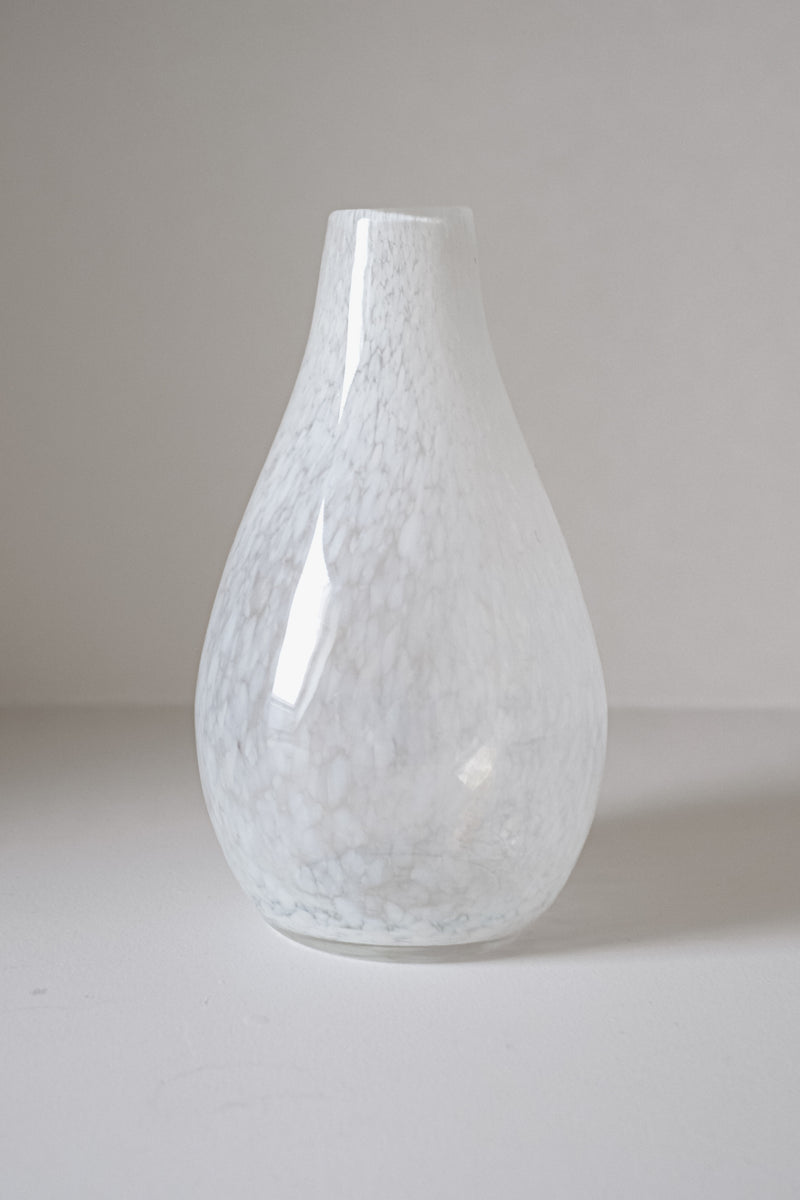 The White Vase Tortoise Glass by septembre studios is a smooth, glossy teardrop-shaped vase with subtle white and light gray marbled patterns, offering a vintage appeal on a plain, neutral background.