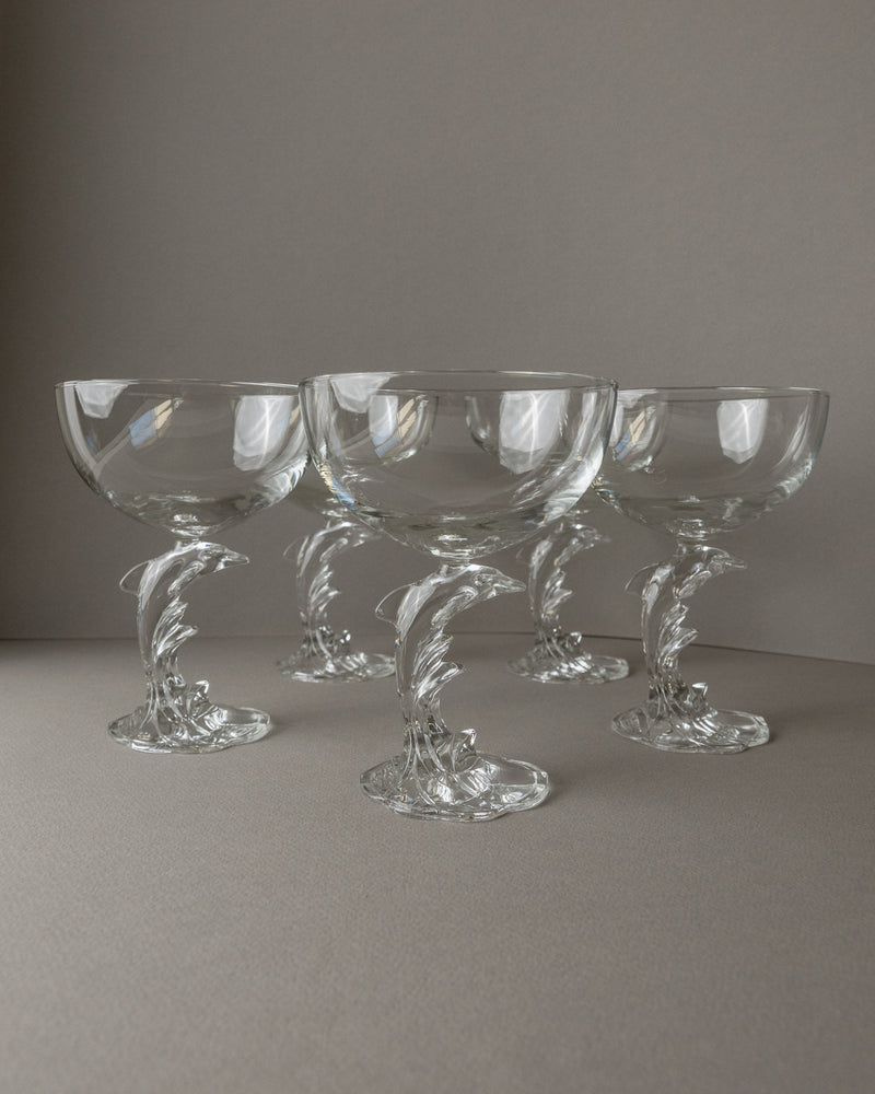 Five Luminarc Delfin Champagne Coupes by Bottega Jacobs showcase elegant glass with intricately designed dolphin-shaped stems, reminiscent of the French 80s collection, set against a neutral background.