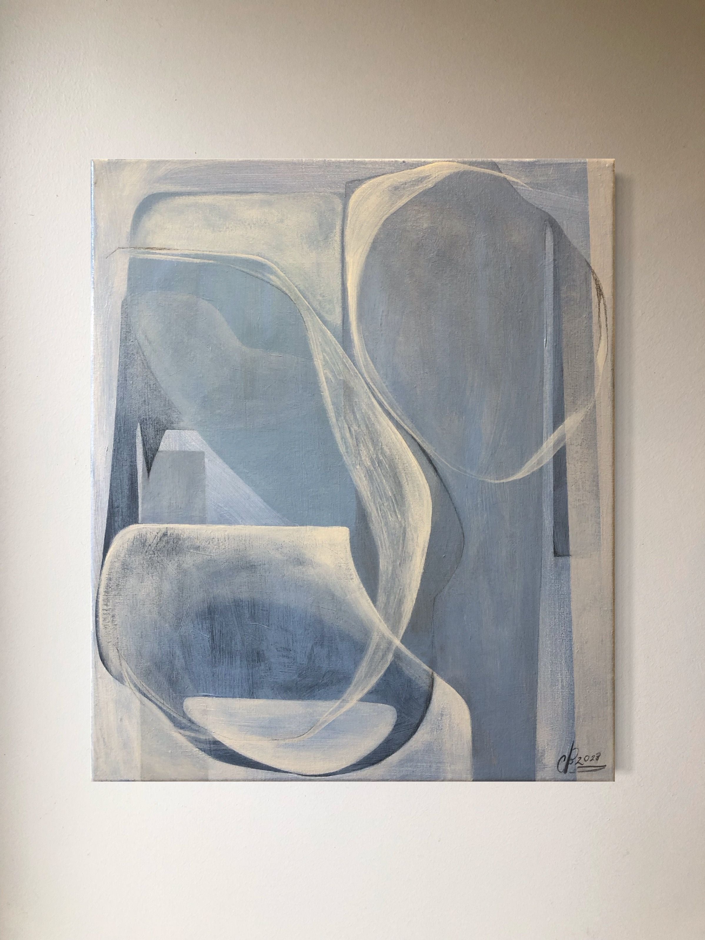 The unframed "In Soft Haze, 2023" painting by Cate Adriana features modern abstract designs with curved and geometric shapes in an array of blue and gray tones. The acrylic composition adds movement and depth to the textured 3D linen canvas, perfectly complementing a plain white wall.