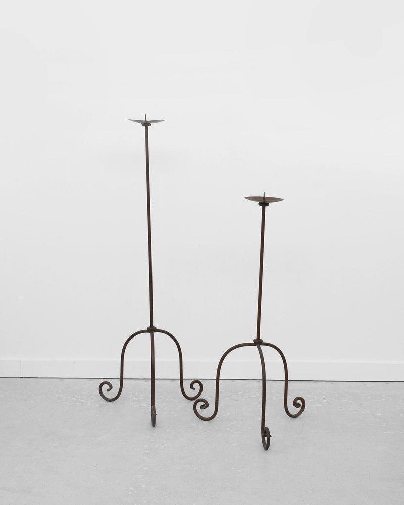 Two iron floor candleholders with curved scrollwork legs, different heights