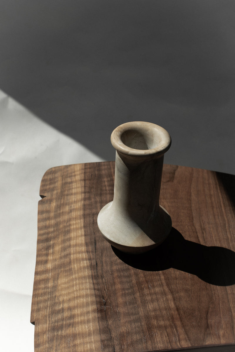 Vintage stone vase detail on walnut wood surface casting shadow