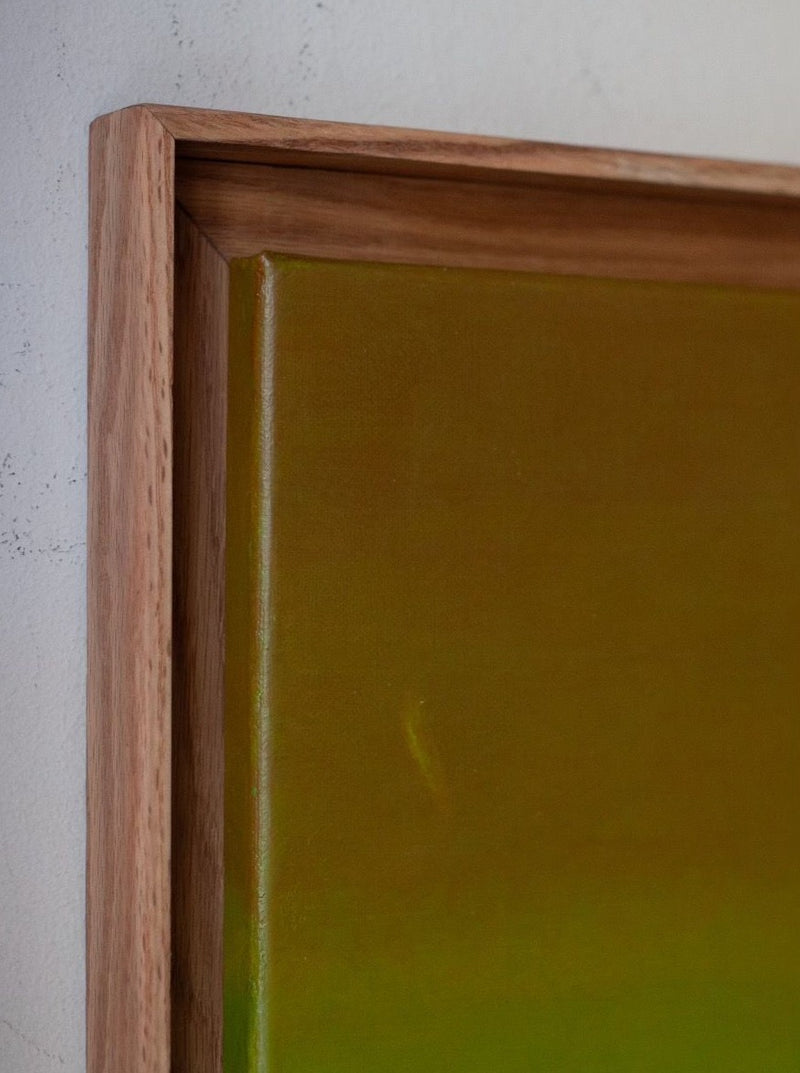 Close-up of an exclusive masterpiece framed with a durable shadow frame. Rebecca von Matérn's "Untitled Acrylic on Canvas, 2024" features a gradient of green and gold hues, perfectly complemented by the frame's simple, natural wood finish. Part of the wall is visible in the background.