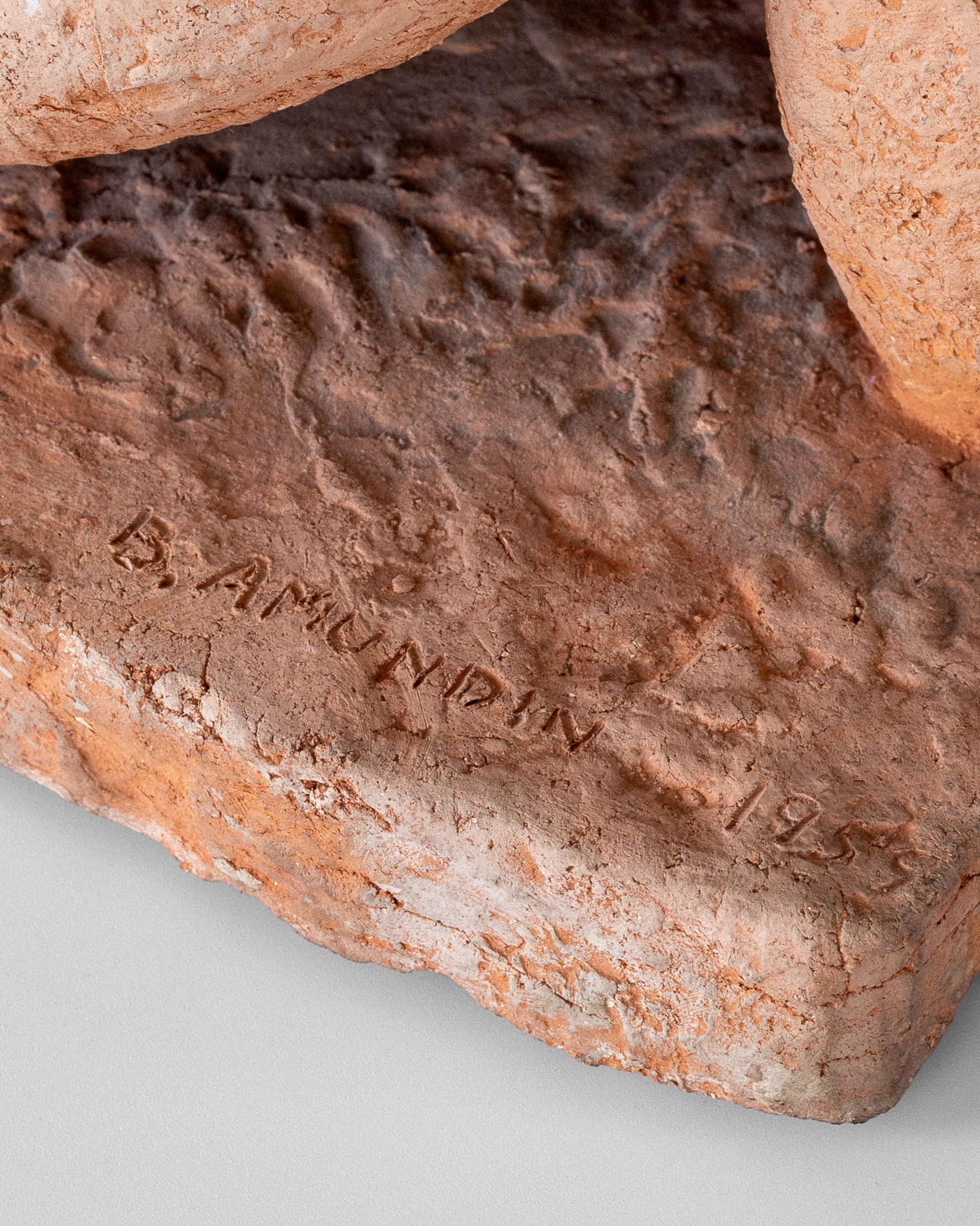 A close examination of the base on the Modernist Terracotta Sculpture by Bengt Amundin, created in the 1950s and offered by Spigel, reveals an engraved signature "B. Amundin 1955." The sculpture's unglazed surface is rough with a distinct reddish-brown hue.