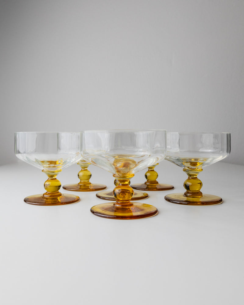 A set of six Bottega Jacobs Murano Glasses, Italy 70s, showcases their transparency and amber accents in a semi-circle on a white surface, evoking vintage charm through subtle color contrast against the plain background.