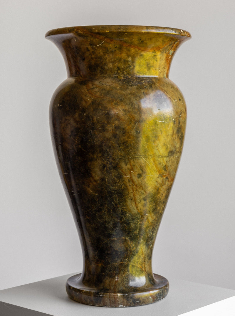 A large Neoclassical Stone Vase by Spigel, boasting a flared rim and an urn-shaped design from the early 1900s, with a rich mix of dark green, brown, and yellow hues on its tall polished marble surface, sits on a white pedestal against a light grey background.