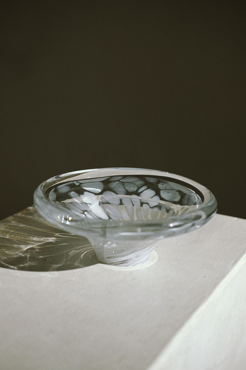 The White Bowl Tortoise Glass by septembre studios features elegant white swirl patterns and sits on a white surface, its shadow visible against a plain, dark background.