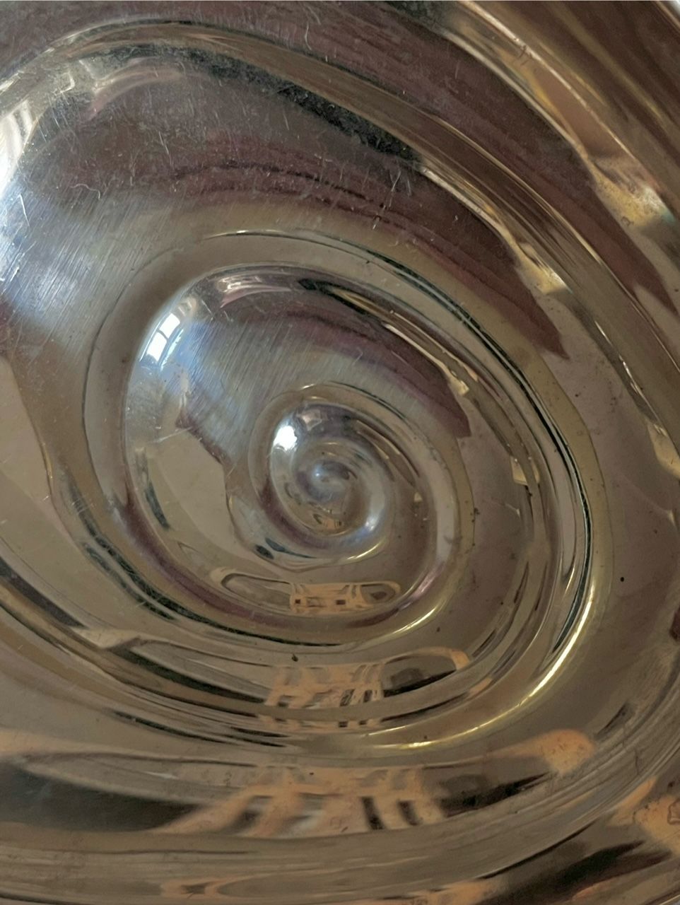 Close-up of a metallic spiral pattern on a reflective surface. The concentric, swirling design creates an illusion of depth, with light reflections and minor scratches visible throughout. This Rare Sterling Silver Midcentury Vide-Poches by Médecine echoes the hypnotic, abstract feel characteristic of a midcentury piece by Tapio Wirkkala.