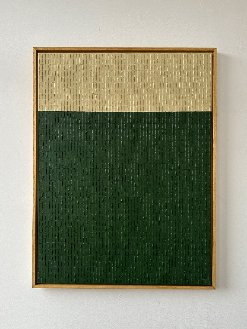 The "Buff Verte" oil on canvas by Roi Elmaliah showcases a minimalist design with two horizontal sections: a wide dark green lower portion and a narrower beige upper portion. The textured canvas is elegantly framed in light wood against a plain white wall, creating the serene ambiance reminiscent of an art gallery in Amsterdam.