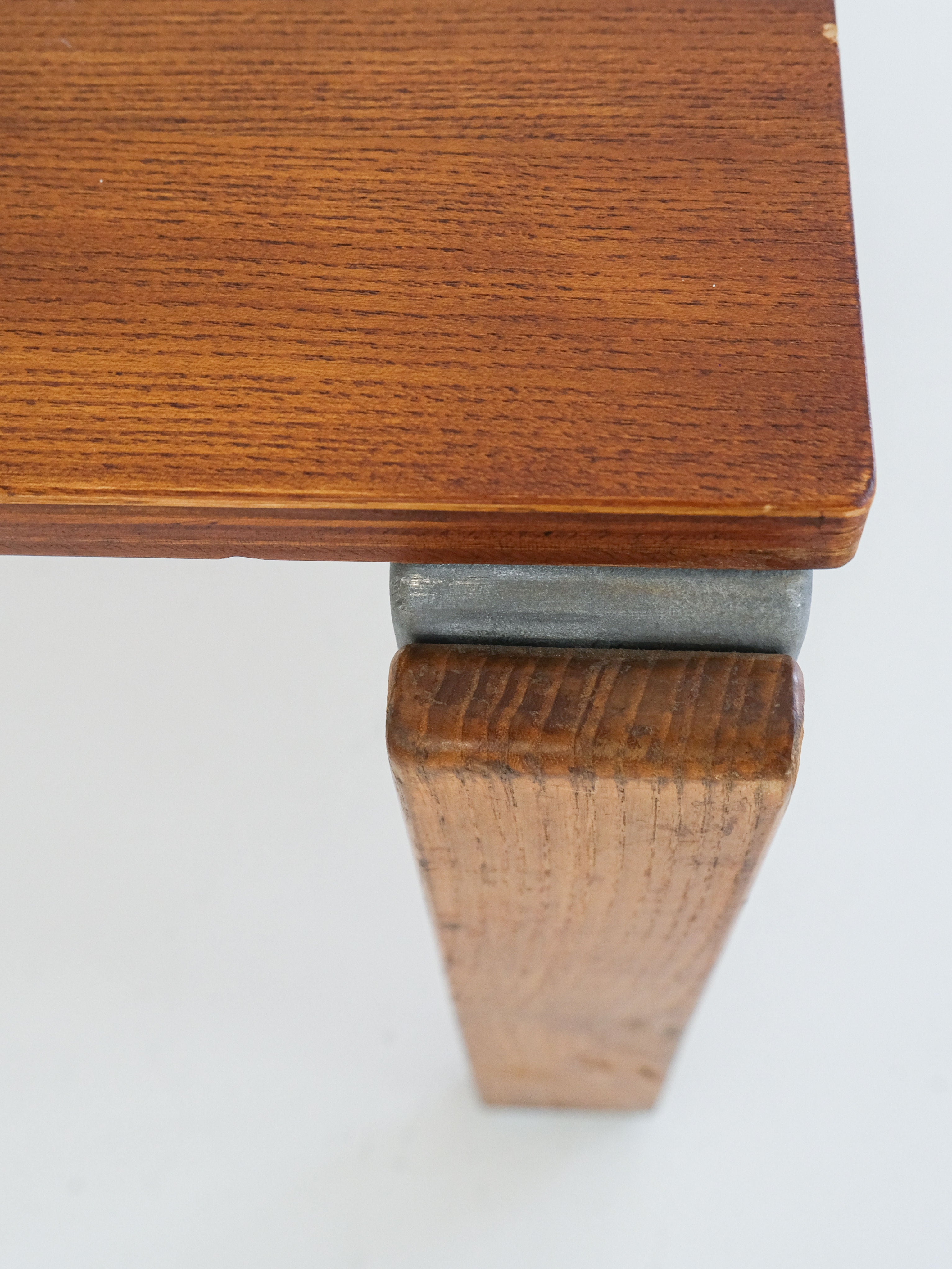 Close-up of a corner on the "Coffee Table by George Candilis and Anja Blomstedt 1970s" from antibeige. Features oak plywood grain, vintage-condition leg attached with a metallic bracket, smooth finish tabletop against a white background.