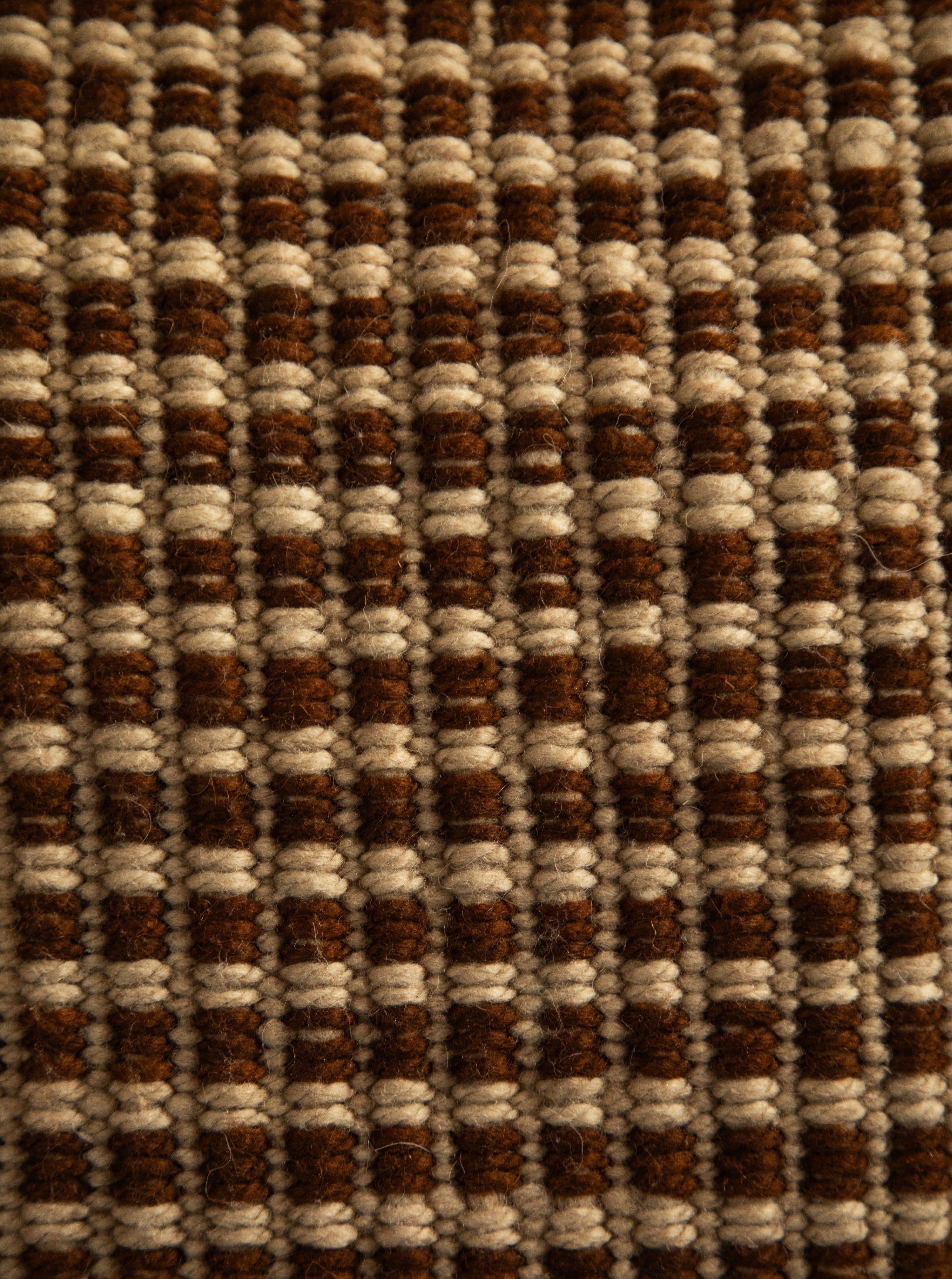 Close-up of a Cima Pillow from Identidad Argentina, showcasing a textured fabric with a striped pattern in shades of brown and cream, featuring a repetitive design made from tightly woven hand-spun sheep wool.