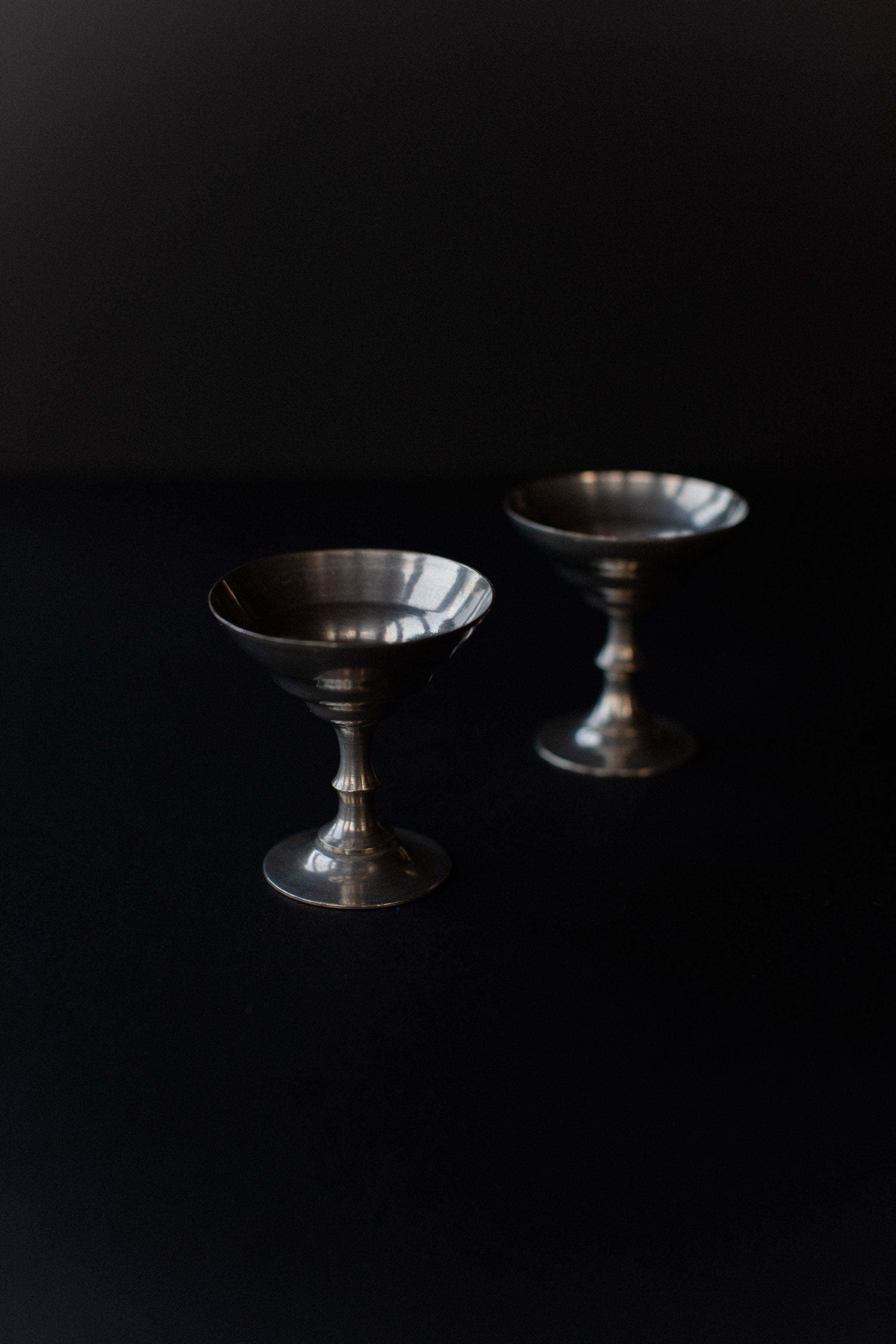 Two Out For Lunch Ice Cream Cups, with a geometric Art Deco design and metallic sheen, are set on a dark surface. The cup in the foreground is clear, while the background cup is slightly blurred, highlighting their elegance against the backdrop.