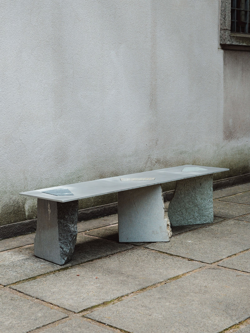 Fragments Milano stone bench with geometric supports on concrete pavement