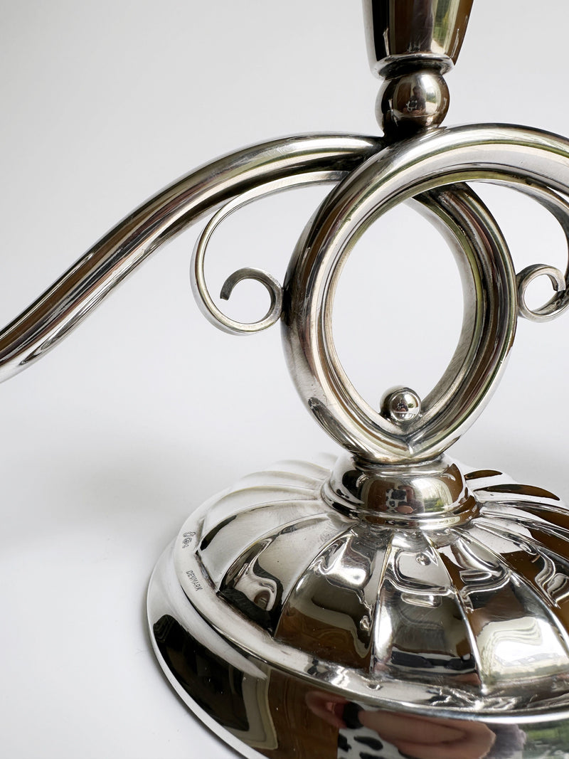 Close-up of a shiny, metallic Danish Mid Century Candleholder by Dodo Vintage, featuring a decorative, swirling filigree design. The candleholder base is detailed with grooves and polished silver plating that reflects light. The background is plain white, emphasizing the intricate and elegant structure of the piece.