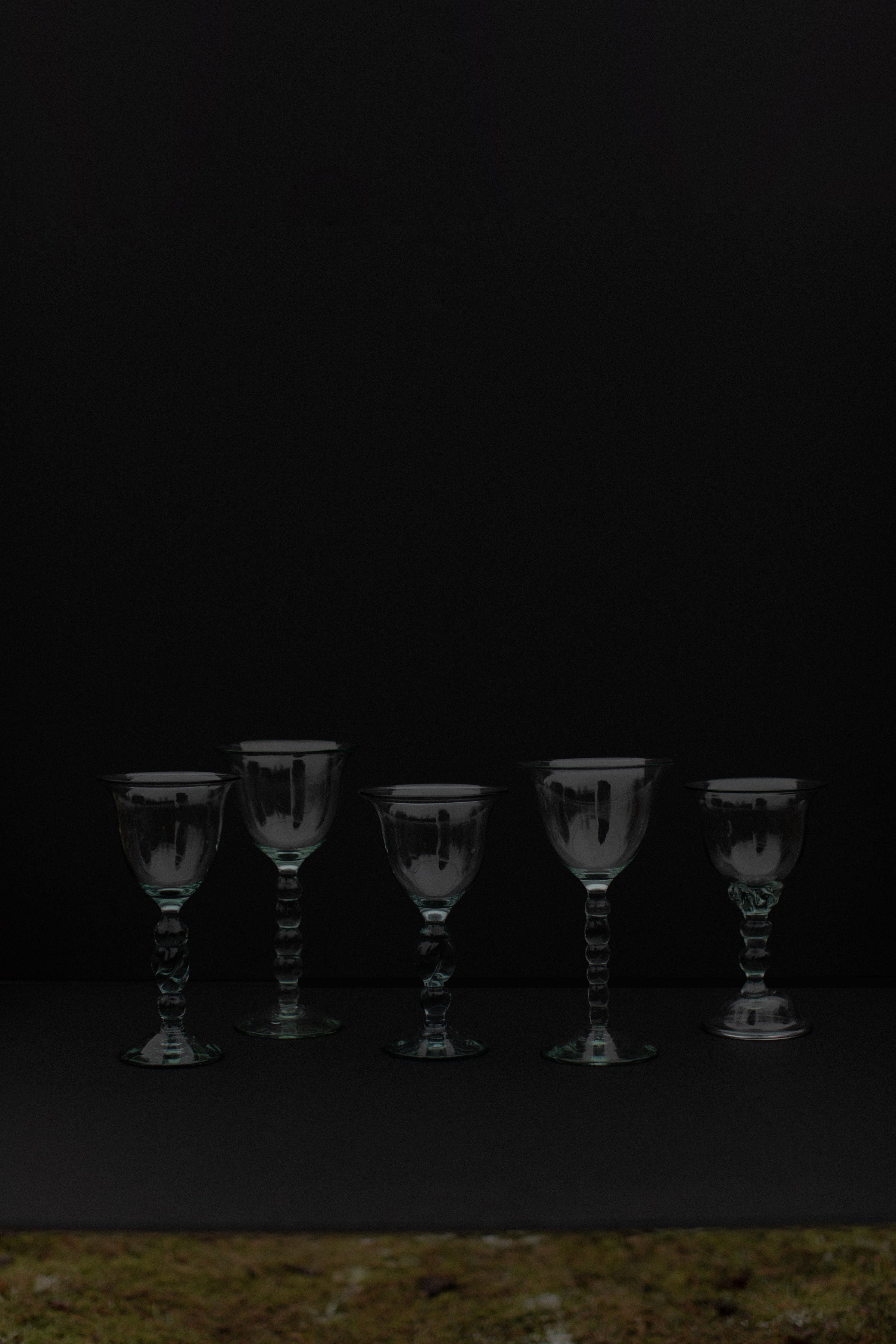 A set of 5 Out For Lunch Handmade Art Glass goblets is arranged in a row against a dark background, with even spacing and their reflections visible on the surface below.