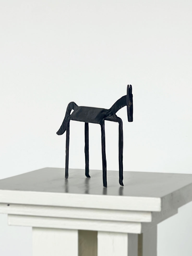 Modern black iron horse sculpture with minimalist design on white pedestal