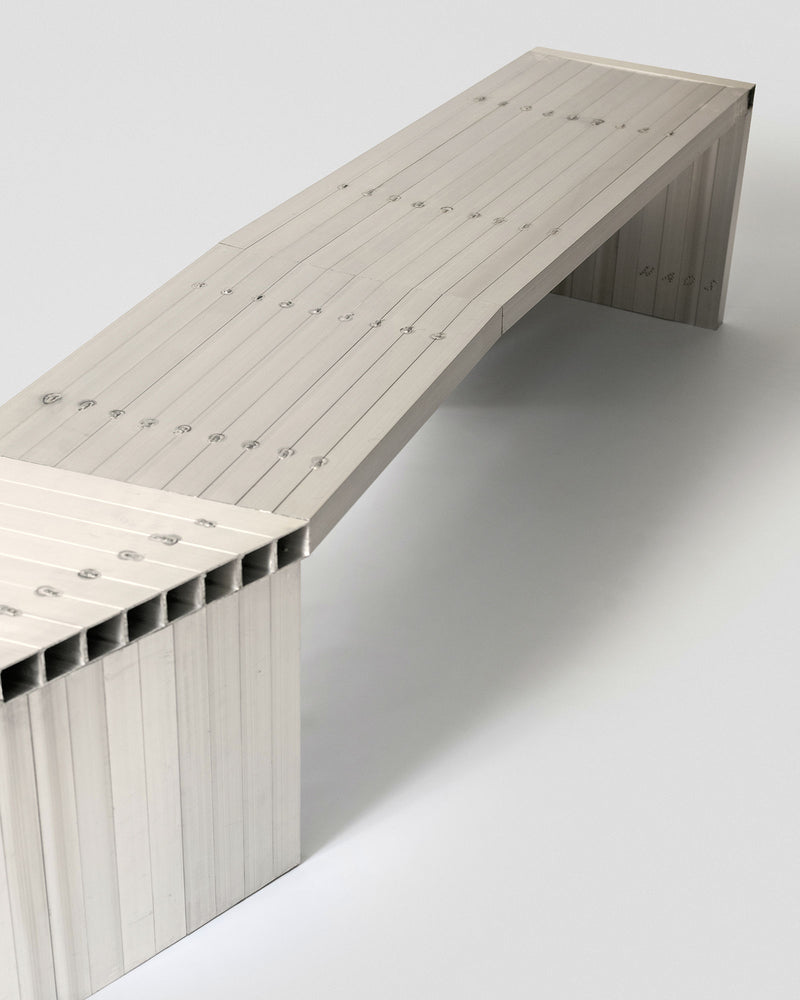 The Aluminum Bench by Studio HAOS features a minimalist, segmented design in light-colored aluminum with visible fasteners, shown against a plain white background—a contemporary statement piece.