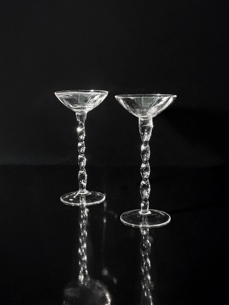 Eight iridescent Art Nouveau liqueur glasses by Dodo Vintage (1910s) are displayed side by side on a reflective black surface, set against a black background.