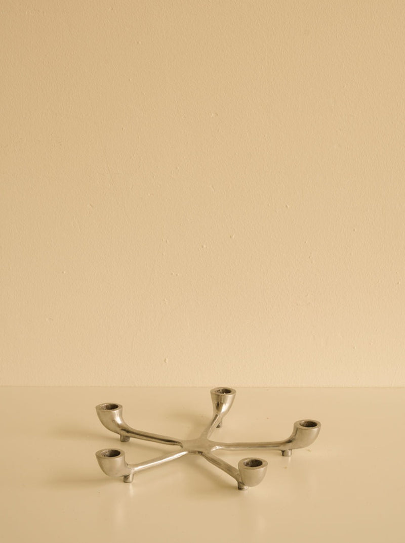 A minimalist image featuring a Les Objets Amsterdam sleek candelabra with multiple branches lying on a smooth cream-colored surface against a matching cream wall.