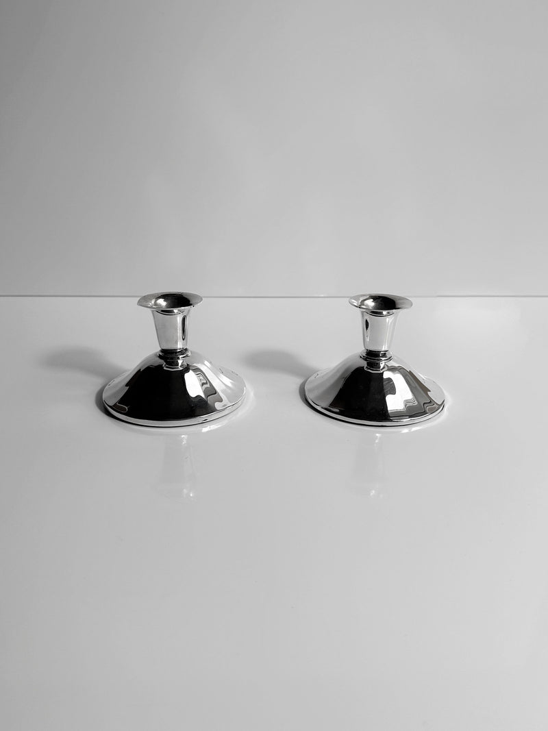 Two Silver-Plated Art Deco Candleholders - 1930 from Dodo Vintage, featuring a sleek faceted design, are elegantly positioned side by side on a glossy white backdrop.