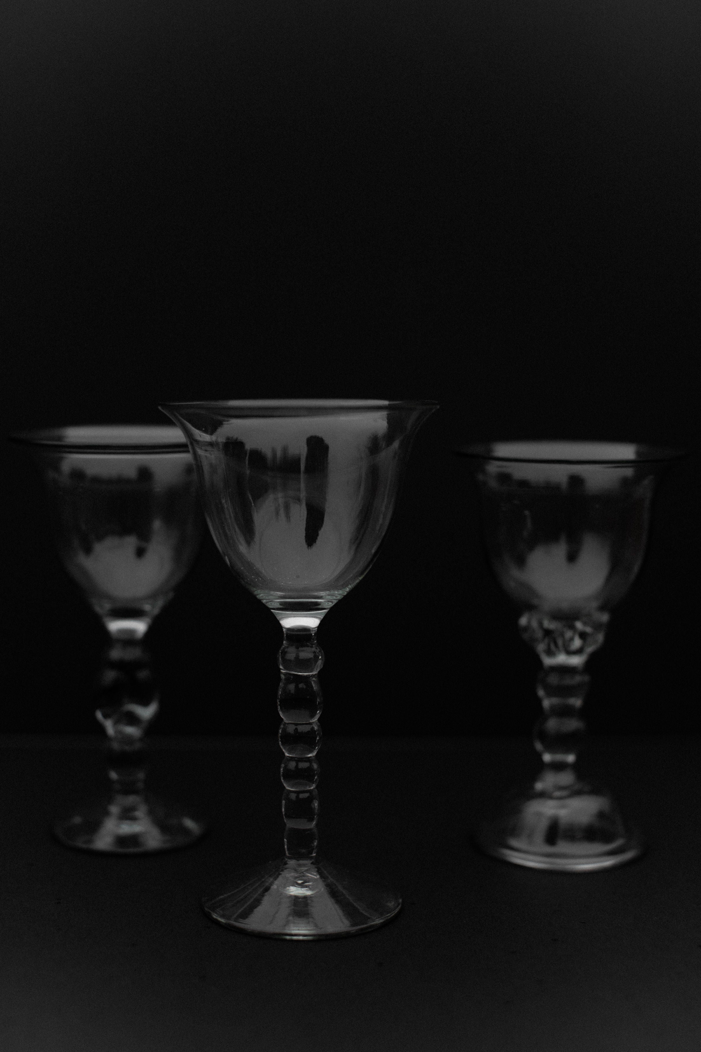 Five elegant, transparent wine glasses from the Out For Lunch Handmade Art Glass set are arranged against a dark background. The central glass is slightly larger and positioned forward, showcasing its artisanal craftsmanship and enhancing the composition's depth and focus.