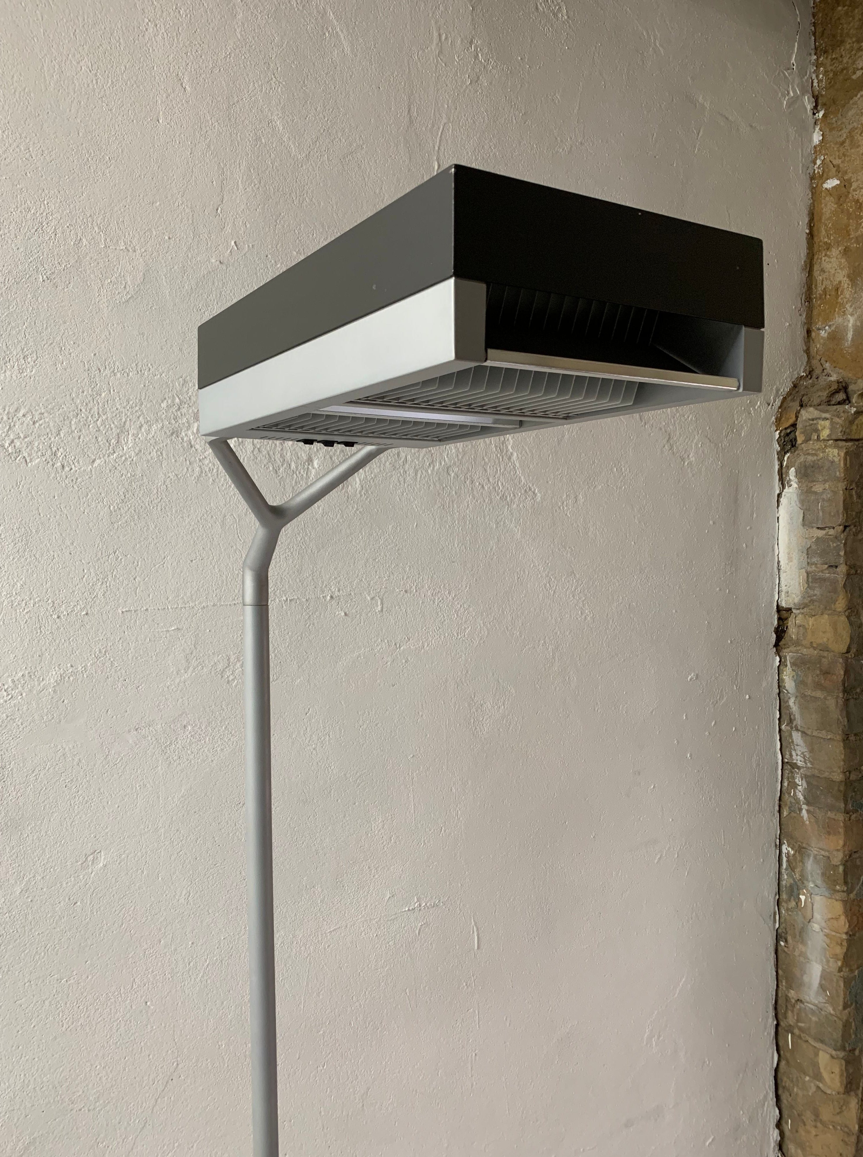 A modern, black and gray air conditioning unit mounted on a gray wall, displaying exposed bricks and a Veter Vintage Postmodern Metal Lamp by Glen Oliver Löw and Antonio Citterio for Ansorg | 1990s on one side.