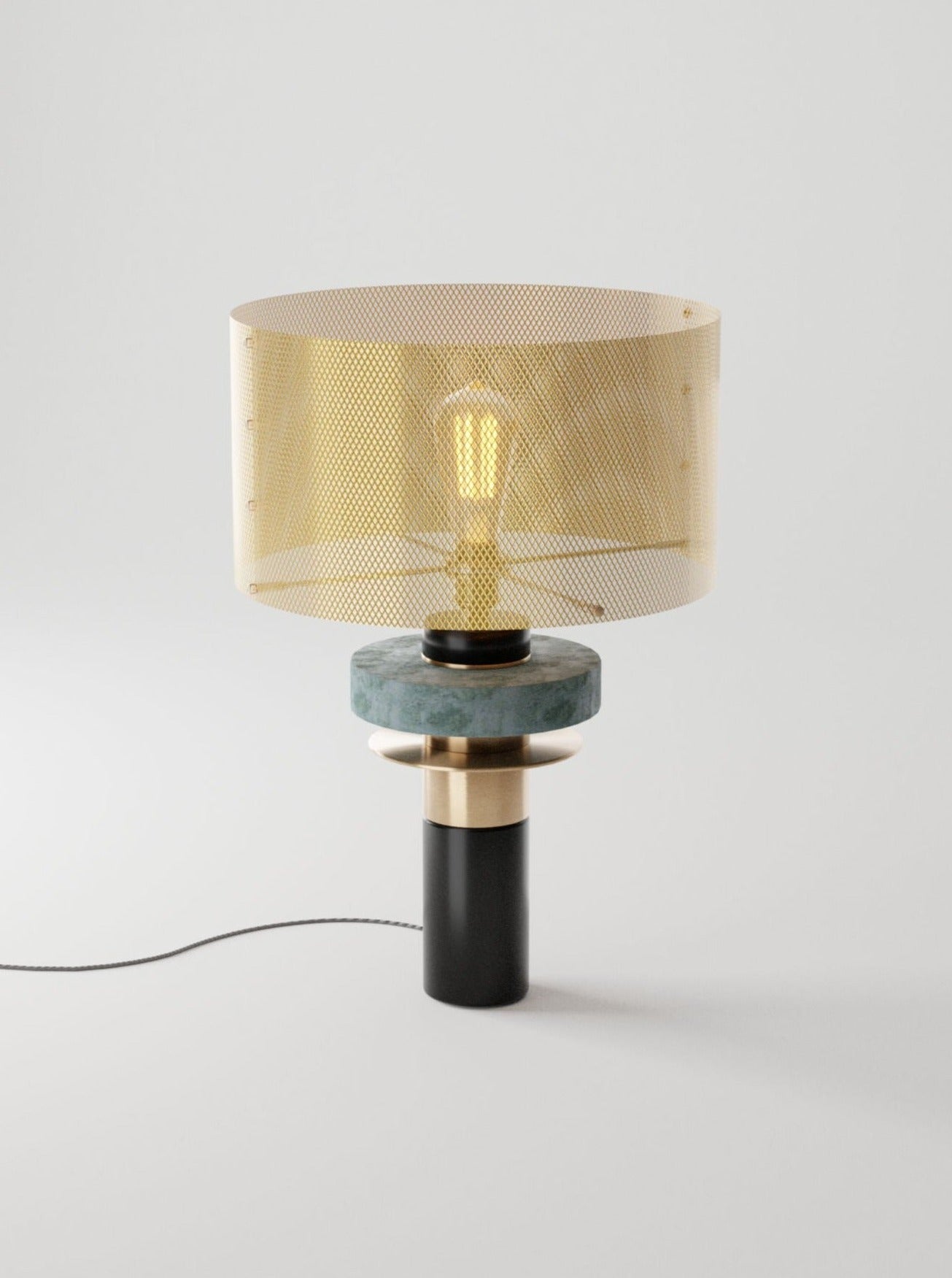 A modern Dyane table lamp by Marine Breynaert featuring a layered base with marble, wood, and solid brass elements, topped by a cylindrical translucent shade with a visible filament bulb.