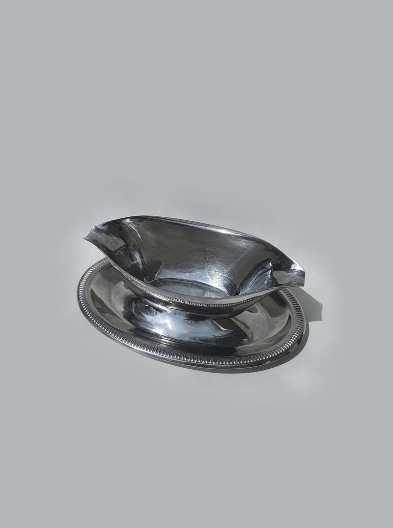 Polished steel gravy boat with decorative rim on matching saucer