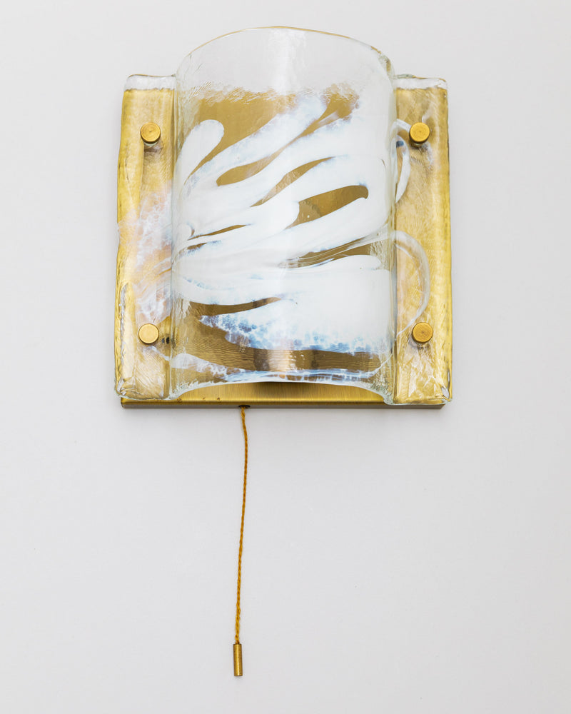A J.T. Kalmar Murano Wall Lamp from the 60s by Bottega Jacobs, featuring a textured glass cover with white swirling patterns, showcases a vintage design. It includes a gilded brass backplate and has a pull-cord extending downwards, set against a simple, light-colored wall background.