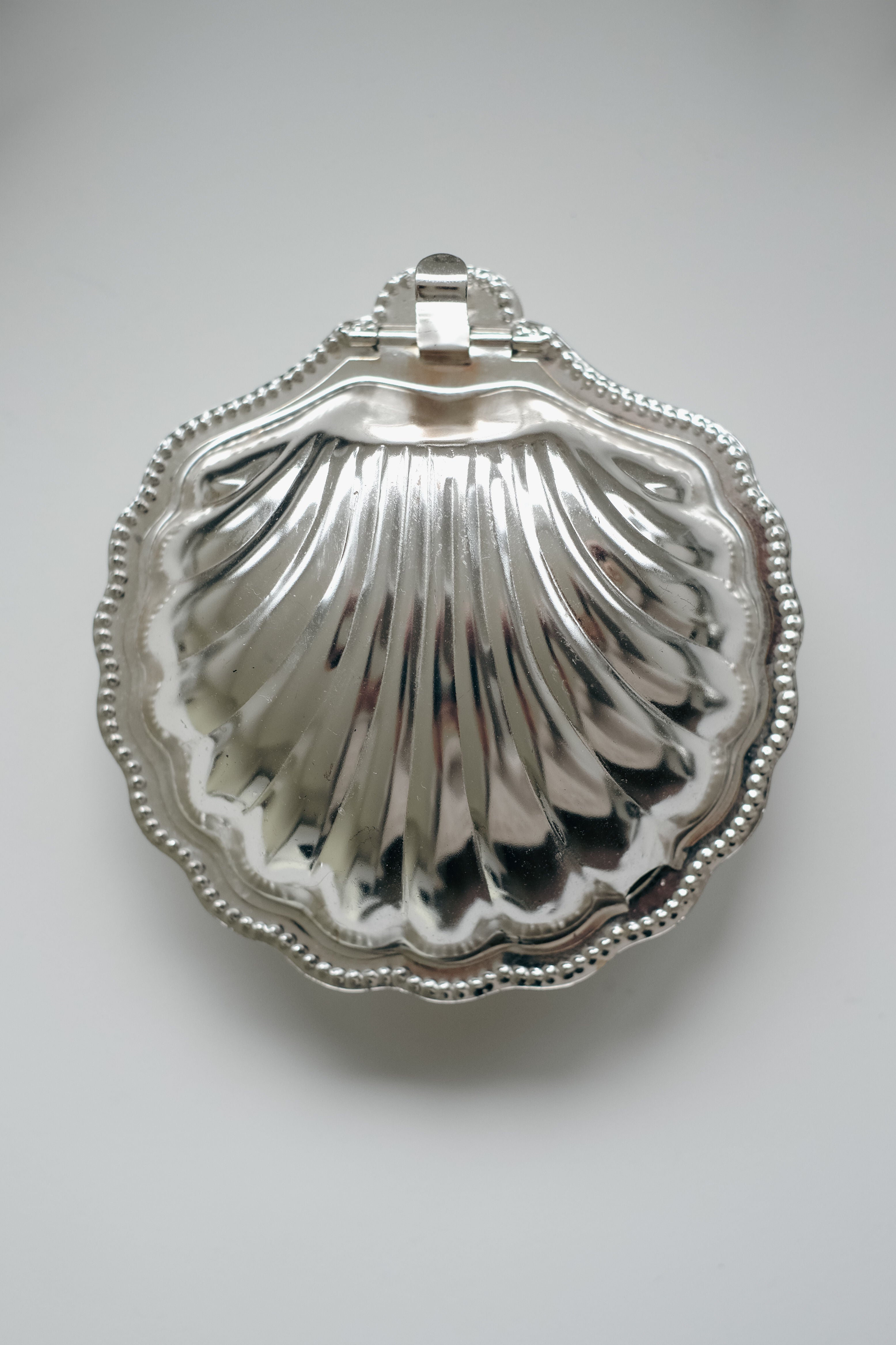 On a plain white background rests the vintage Shell Shaped Butter Dish by septembre studios, crafted from silver with a ribbed pattern and beaded edges.