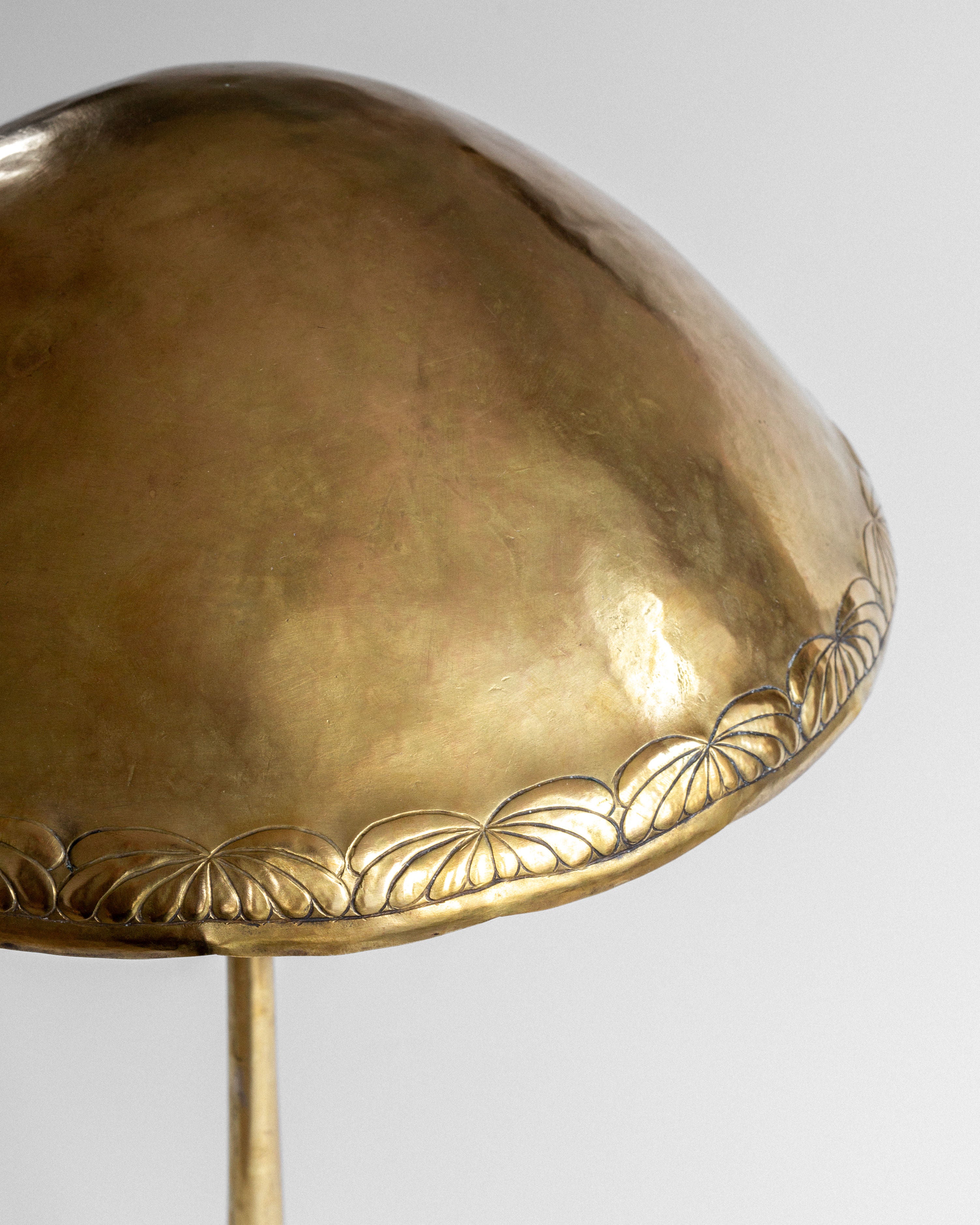 Close-up of the Spigel Art Nouveau Brass Table Lamp's antique dome-shaped gold lampshade, featuring floral engravings on the edge. It has a polished, reflective finish against a plain light gray background.