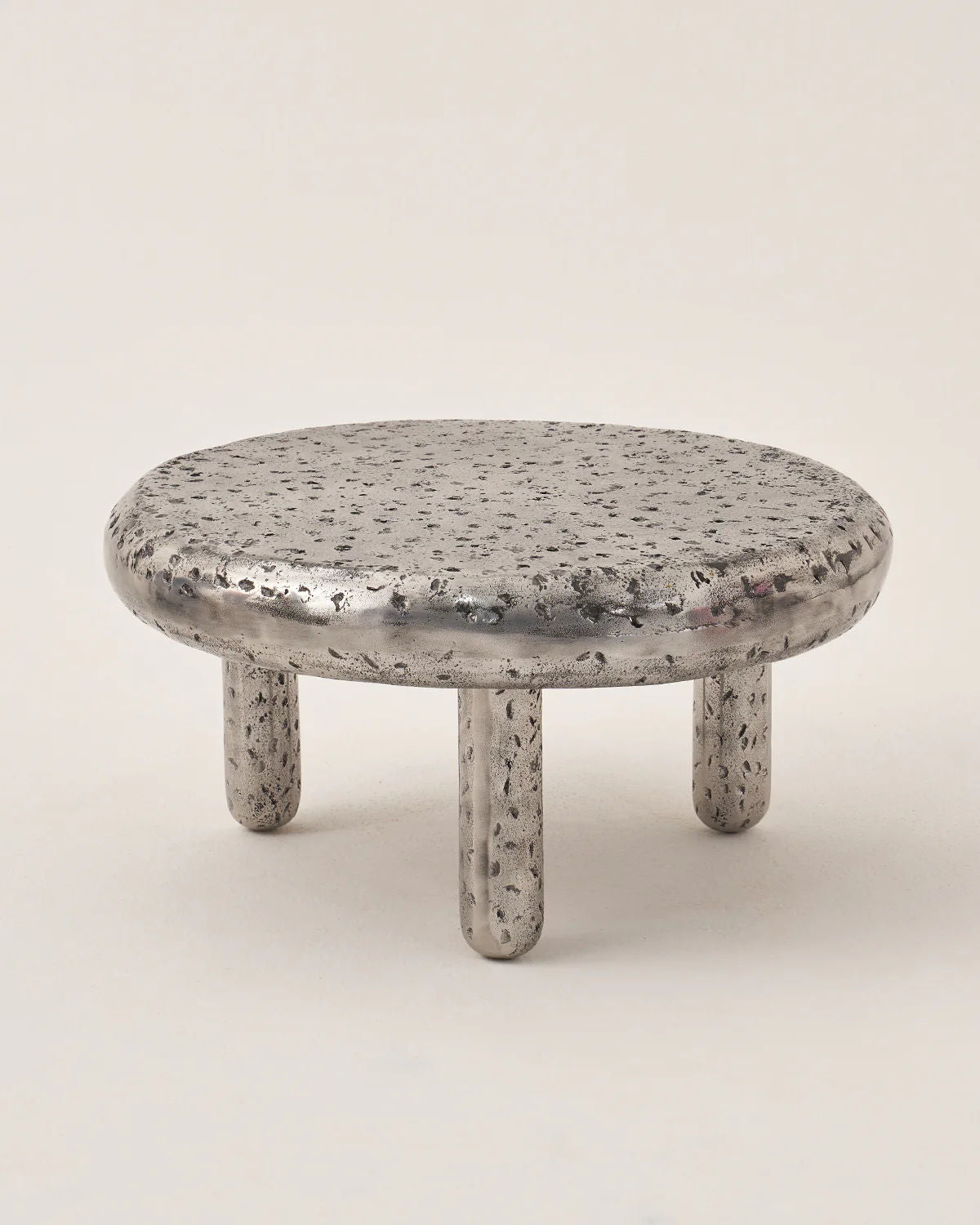 The LMNOH "Crater" set of two features round, low metal tables with a textured, dappled surface like a lunar landscape and four short legs against a plain background.