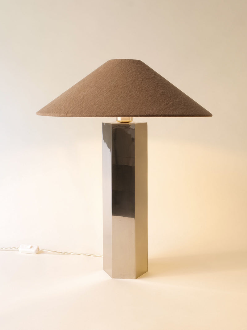 The Grand Hexagonal Lamp by Collection apart features a tall stainless steel base and a wide brown conical fabric shade, bringing stylish 1970s retro flair to any space. Displayed on a light surface against a neutral background.