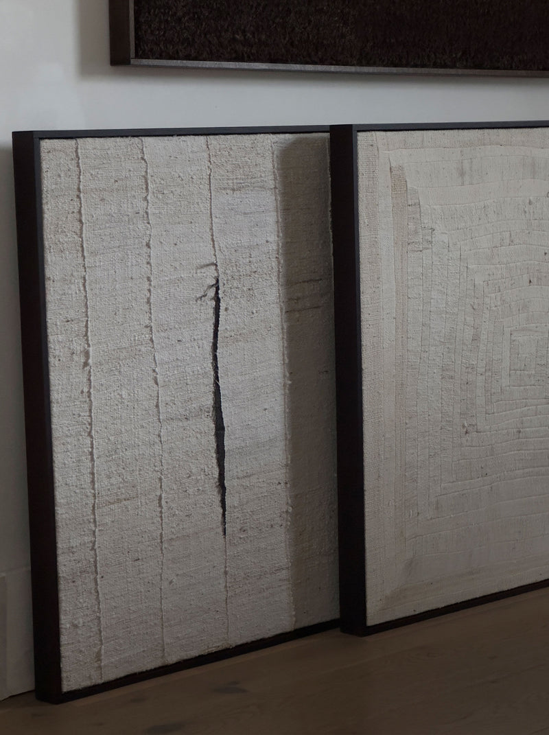 Two framed "Mast, 2024" artworks by Bec Kirby are leaning against a wall, crafted in solid oak. The left piece showcases vertical textured lines with a central dark crack, evoking the look of handwoven kapok fibre cloth. The right piece features concentric rectangular patterns with subtle texture variations in muted tones.