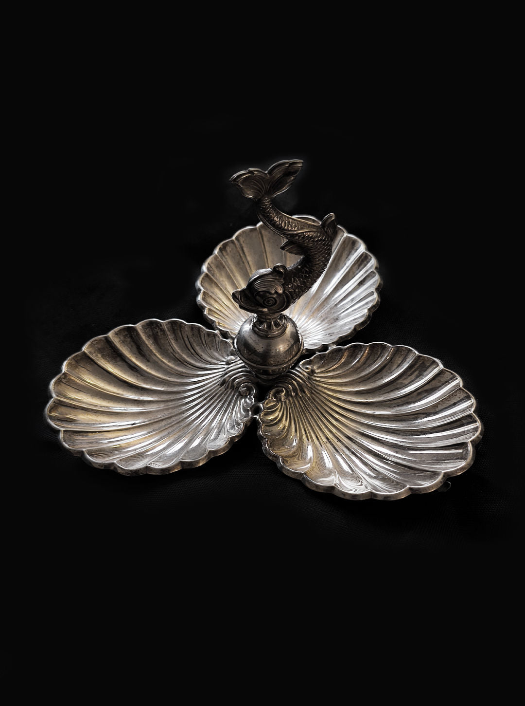 The Les Objoies Shell & Fish Triple Tray features a silver-plated design with three shell-shaped compartments and a fish-shaped handle, set against a dark background.