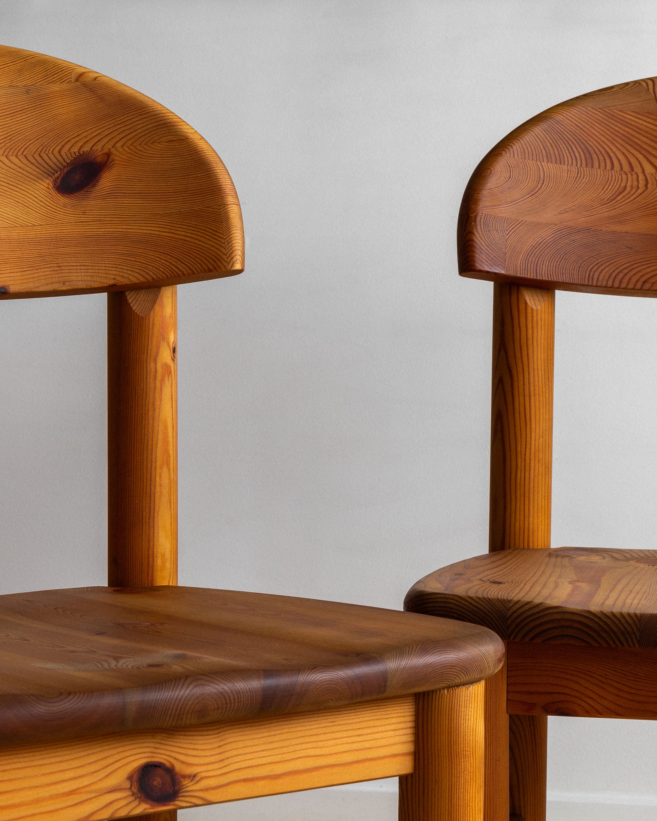 Two Spigel 4 Pine Chairs by Rainer Daumiller, featuring rounded backs and seats, are placed side by side against a plain white background. Crafted from solid pine in the 1970s, they showcase a smooth, polished finish that highlights the wood grain and knots, giving them a natural, rustic appearance reminiscent of Danish design.