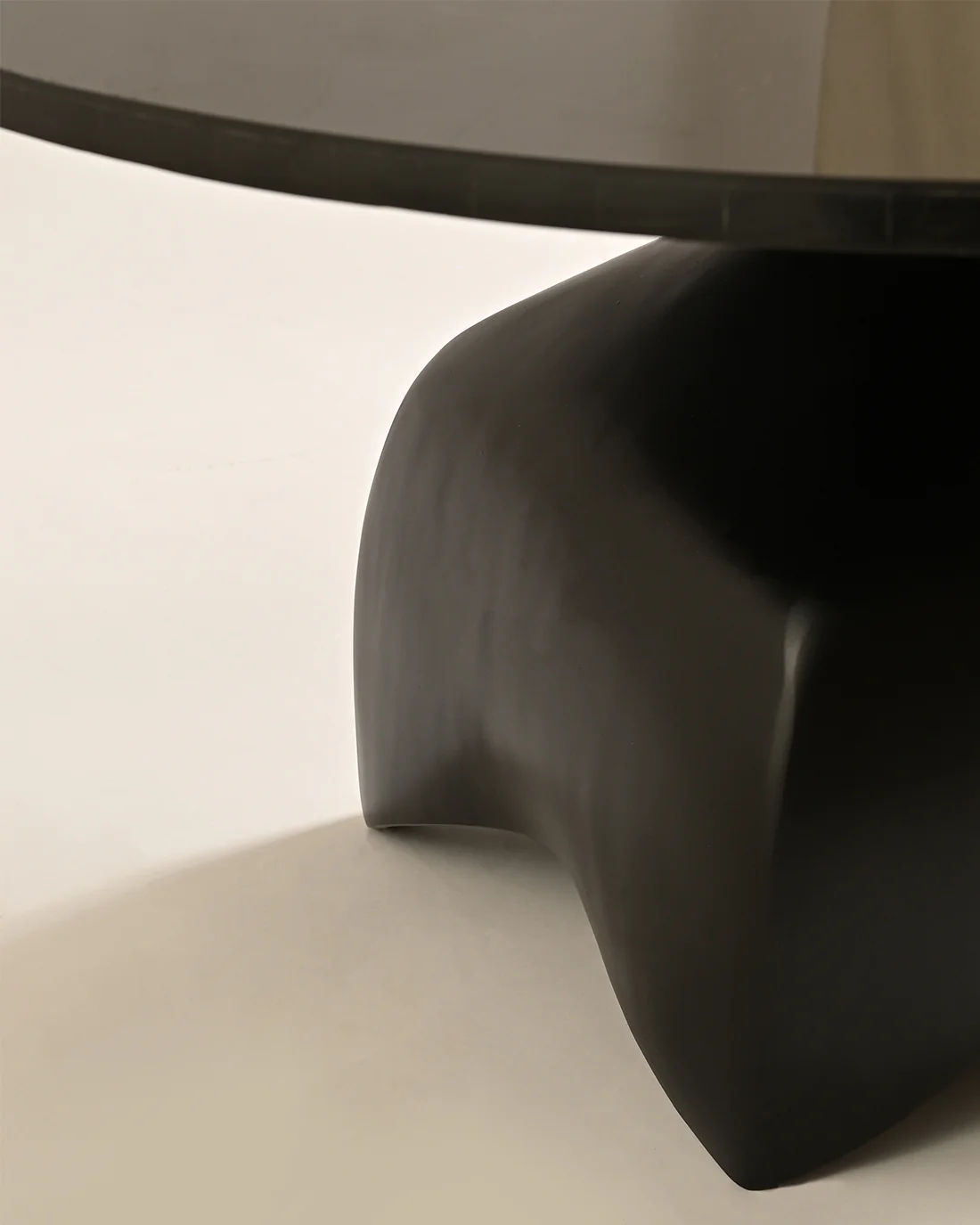 A close-up of the LMNOH Jasper Coffee Table showcases its modern design, with a smooth, rounded black casted aluminum base and a glossy dark tabletop. Its minimalist style starkly contrasts against the light-colored floor.