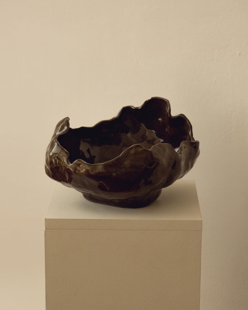 Dark bronze sculptural bowl with irregular organic edges on white pedestal