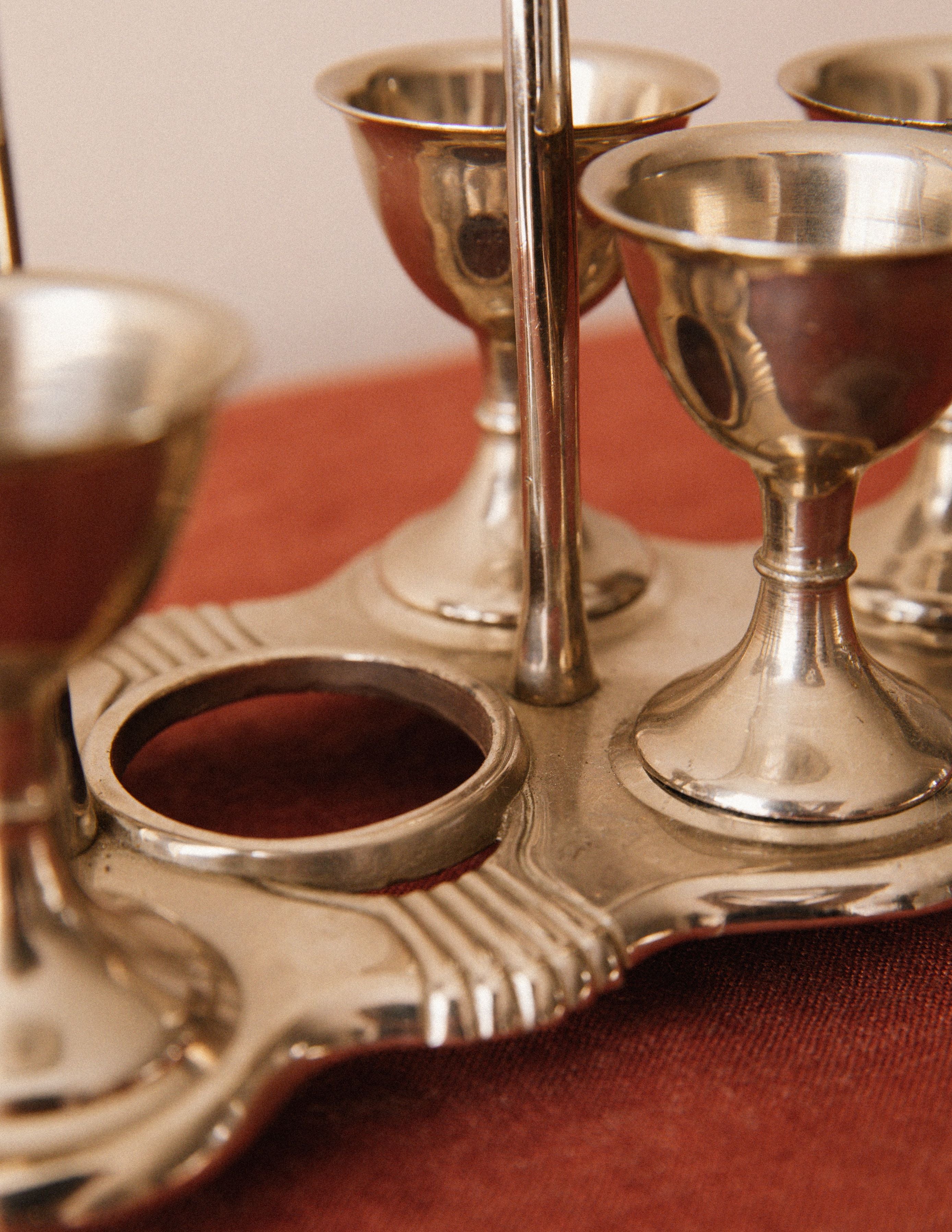 Close-up of the Vintage Egg Cruet Holder Set by Arcā Collections, featuring four sculpted silver-plated cups, displayed as a unique tabletop accent on a reddish-brown textured surface.