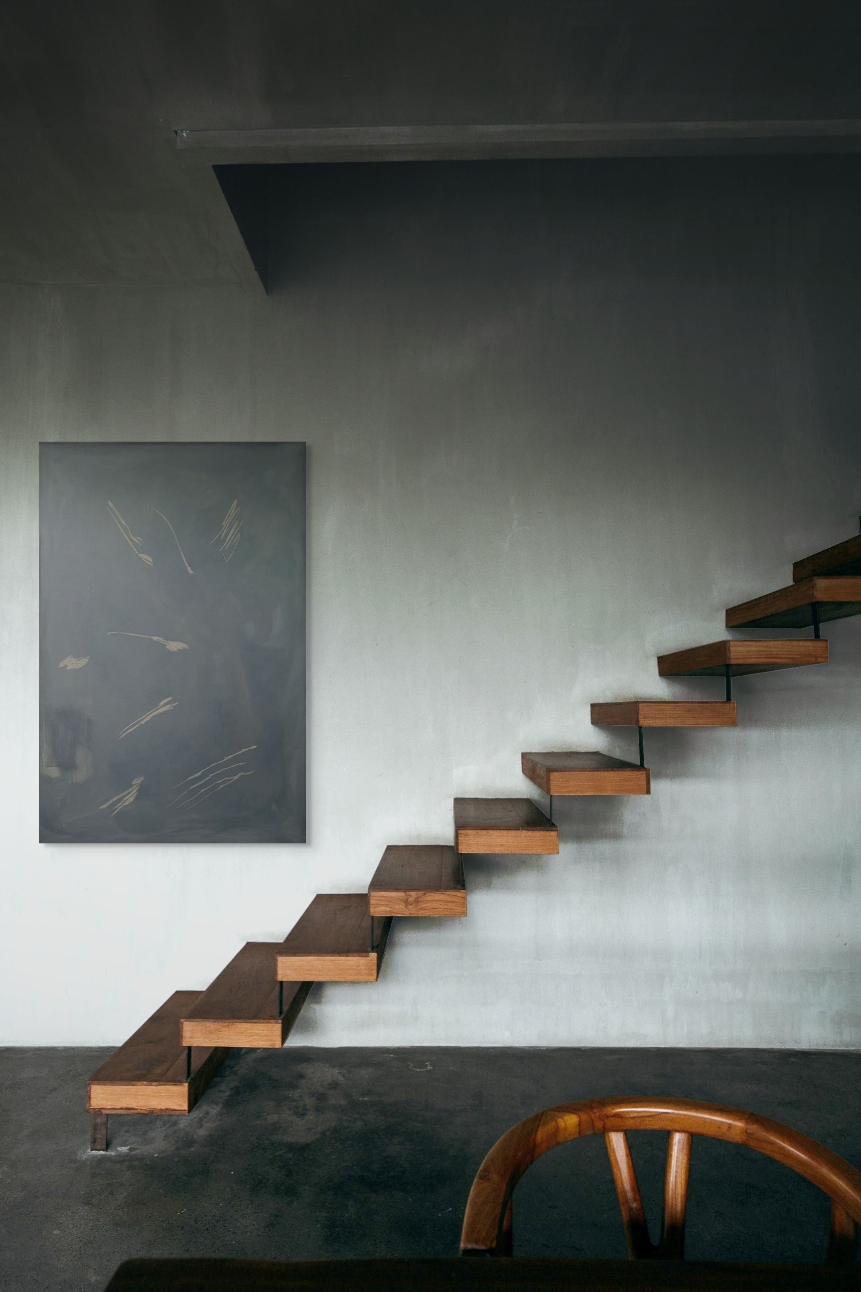 A modern staircase with wooden floating steps lines a grey wall beside the 'I am rooted, but I flow' painting by Yeliza Gevorgyan. A curved wooden chair is partially visible in the foreground.