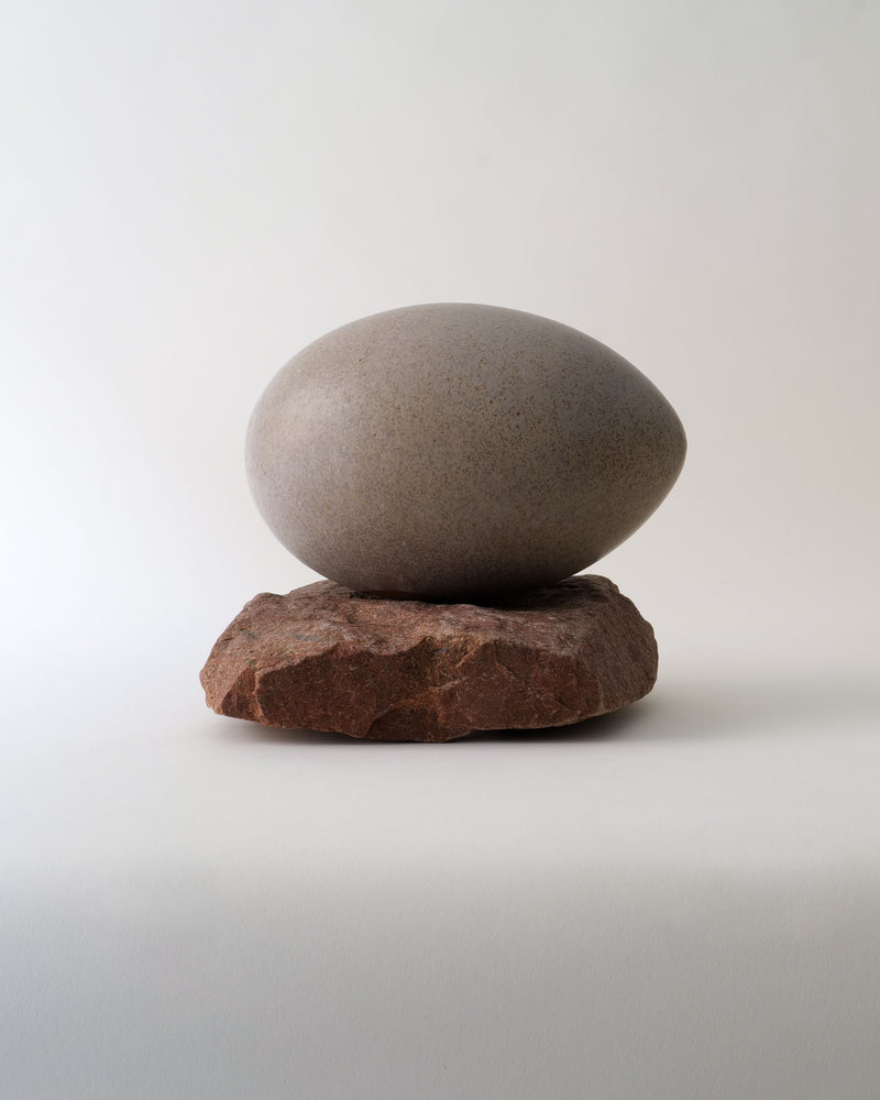 Large grey ceramic egg sculpture balanced on rough brown stone base